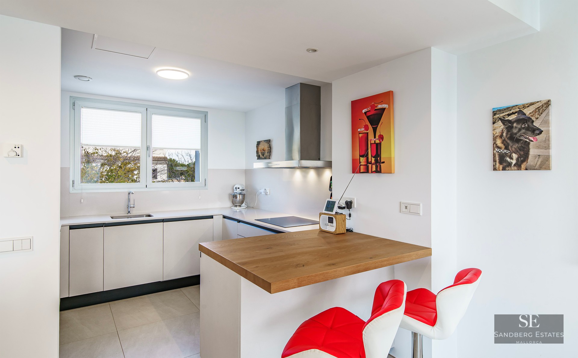 Bright modern kitchen featuring white cabinets, a wooden breakfast bar with red stools, and stainless steel appliances.