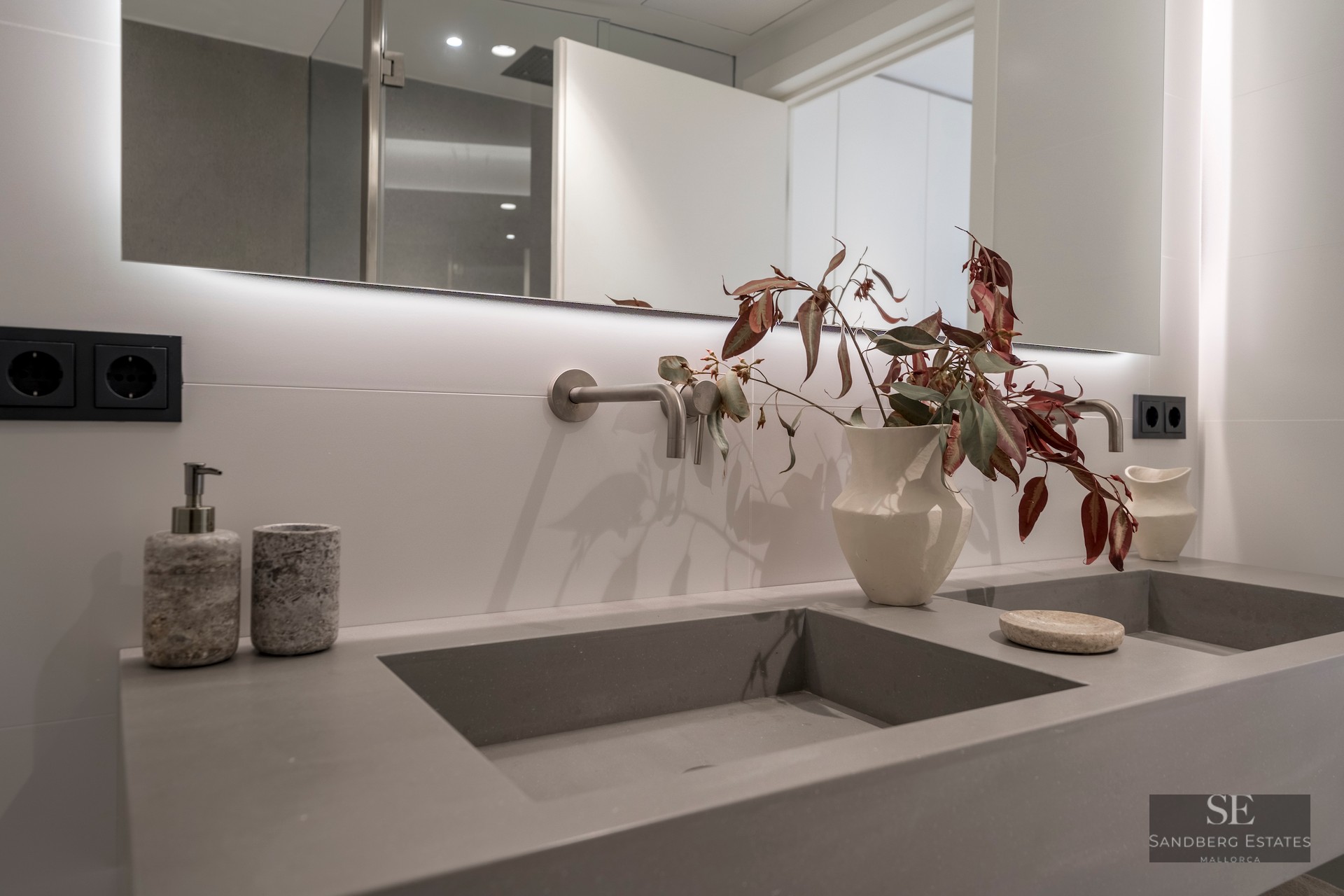 Gray integrated dual sinks with wall-mounted faucets and a large backlit mirror in a modern bathroom.