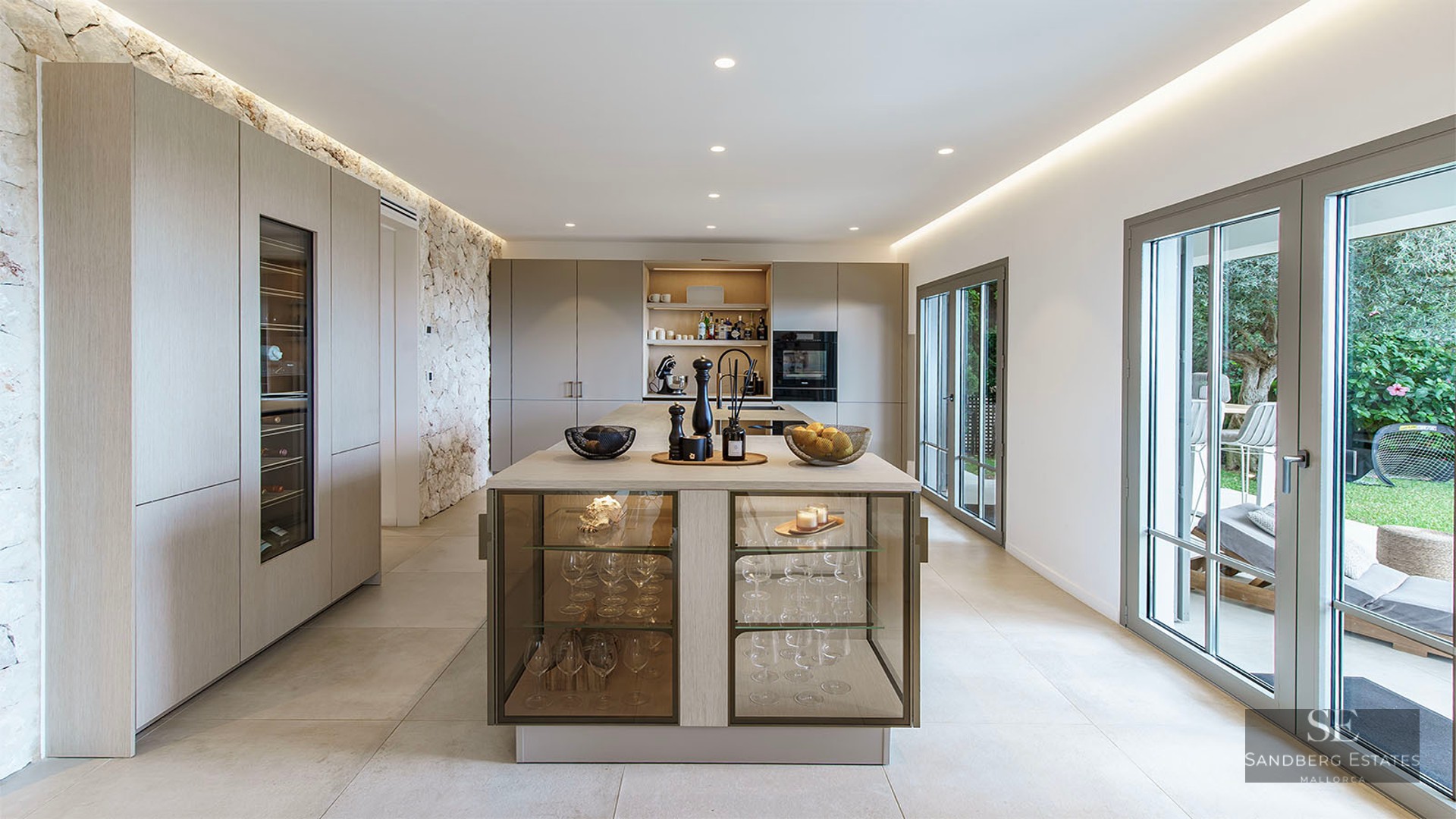 Spacious contemporary kitchen featuring a large island, integrated wine cooler, natural stone wall, and garden access.