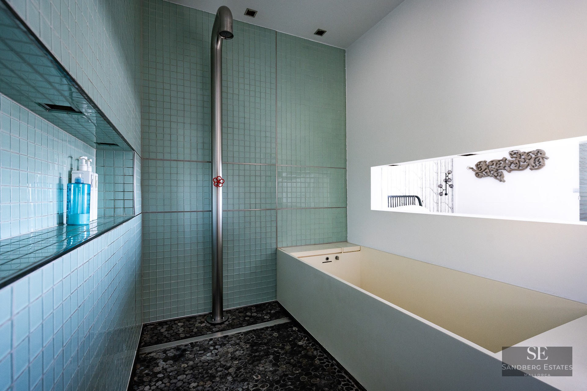 Modern wet room featuring mint green mosaic tiles, a minimalist stainless steel shower, and a pebble floor.