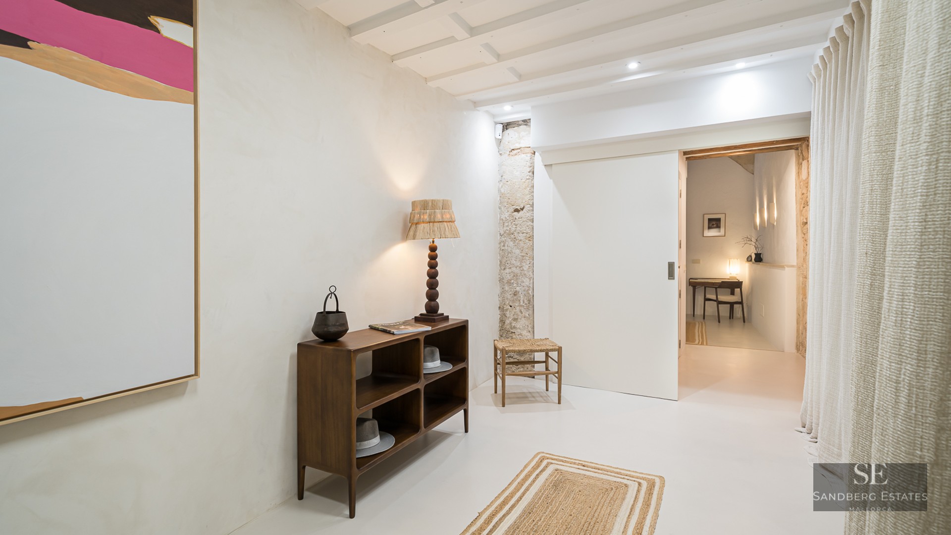 Minimalist hallway featuring a wooden console, designer lamp, abstract art, and an exposed stone pillar.
