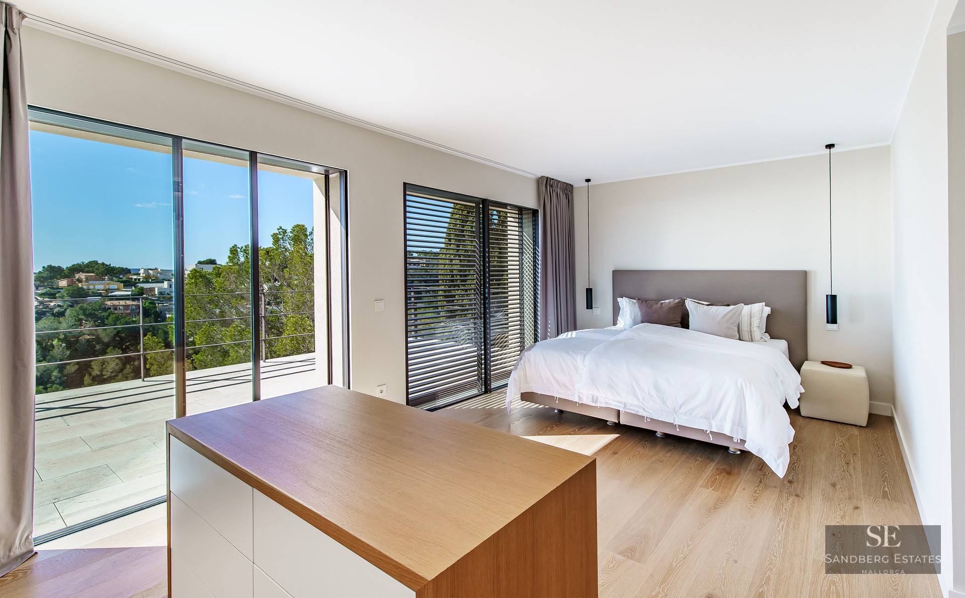 Bright master bedroom featuring wooden floors, a large bed, and floor-to-ceiling sliding glass doors opening to a terrace.
