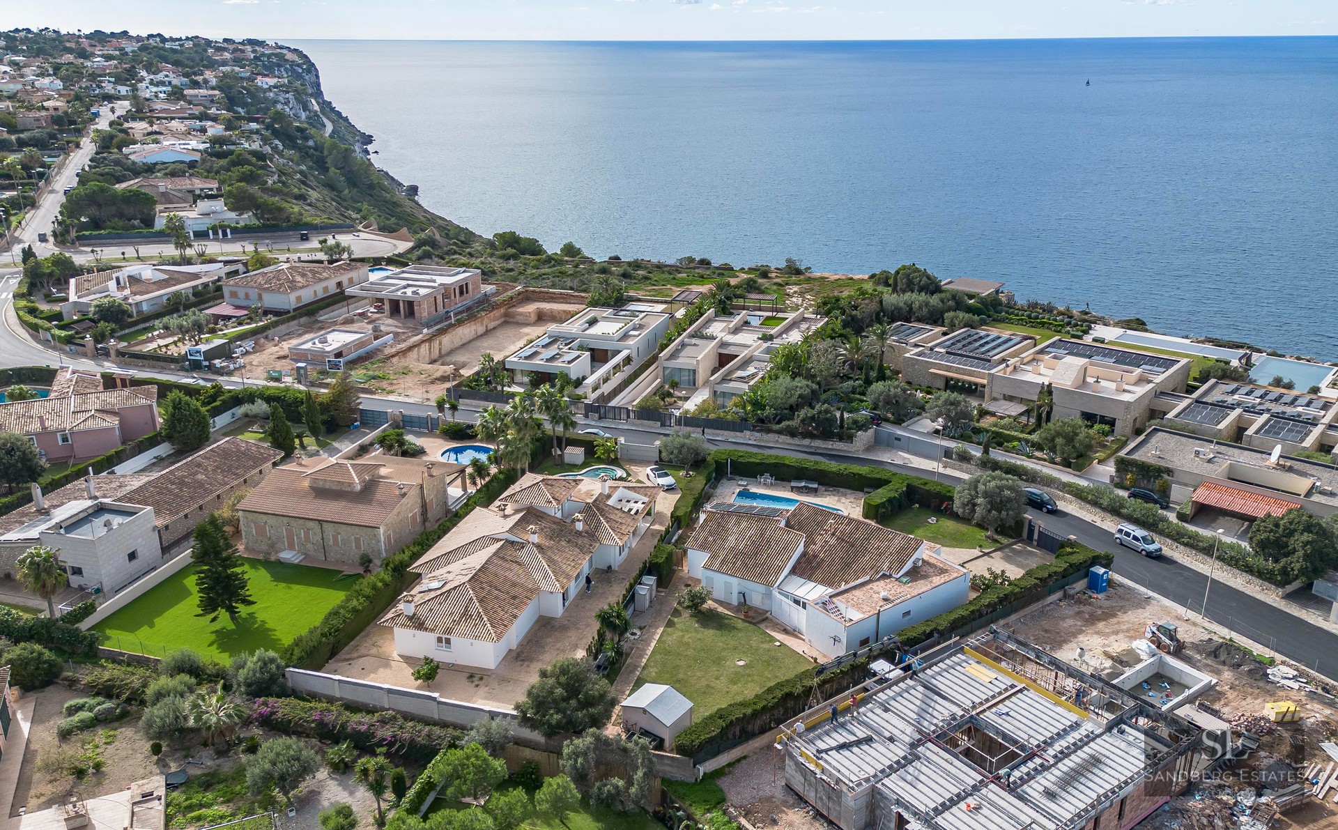 High-angle aerial view of an exclusive coastal residential area with Mediterranean villas, private pools, and sea views.