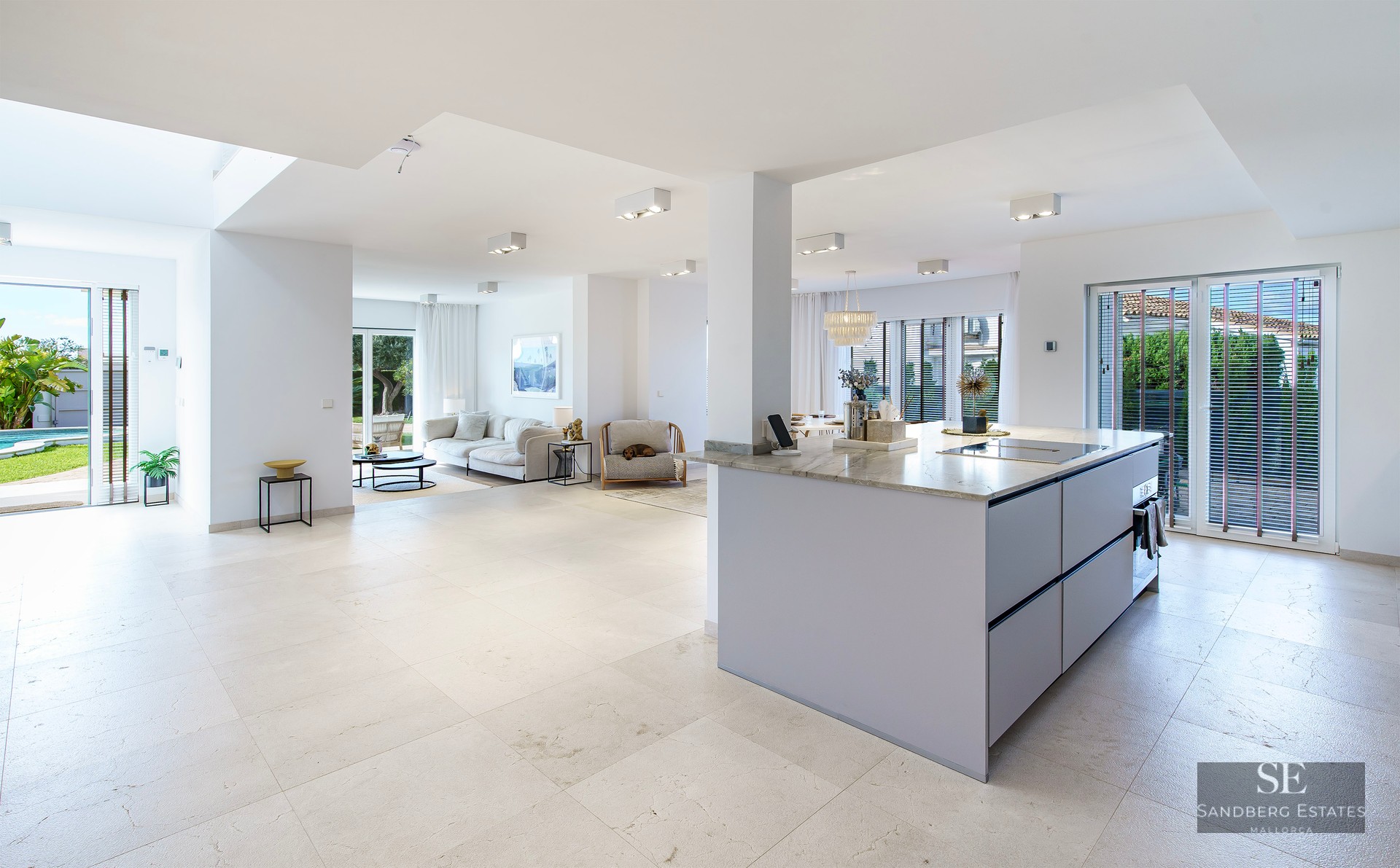 Bright open-plan living room with white sofa, marble kitchen island, and large glass doors leading to a garden.