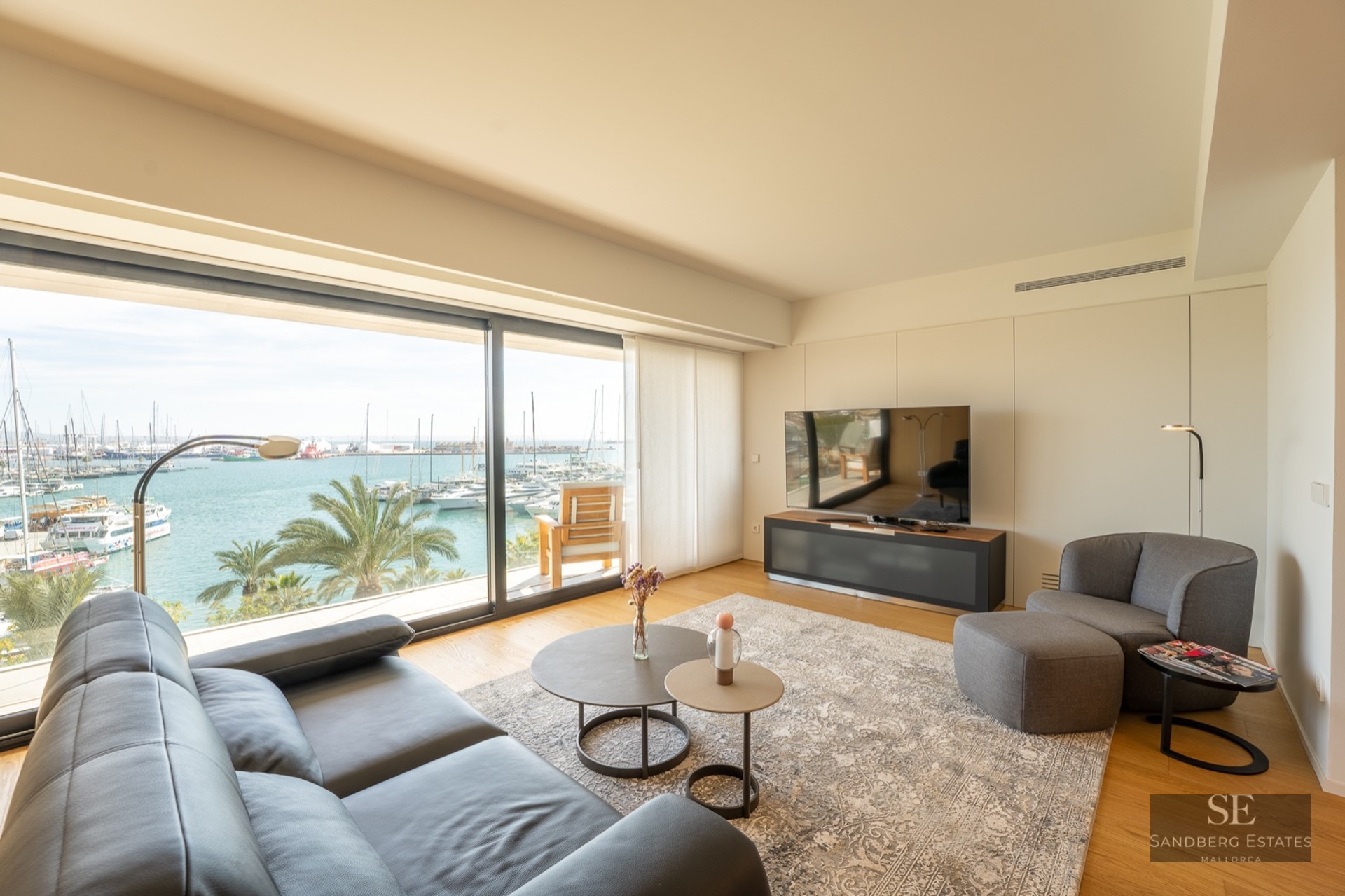 Bright modern living room with a black leather sofa and large windows overlooking a sunny marina with boats.