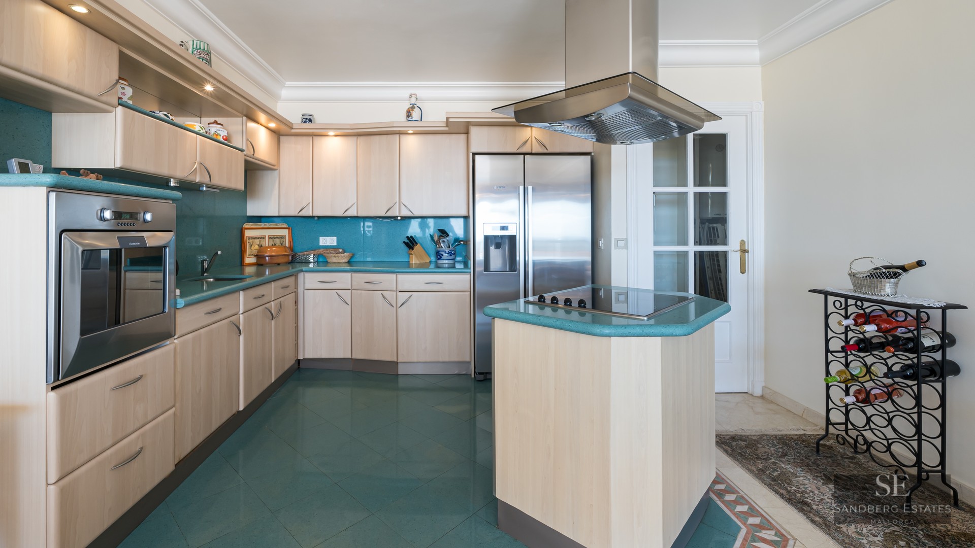 Contemporary kitchen with light wood cabinets, turquoise countertops and floors, and stainless steel appliances.
