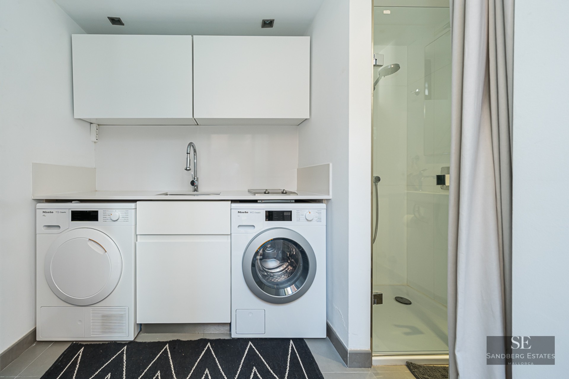 White laundry nook with Miele washer and dryer next to a glass-enclosed walk-in shower.