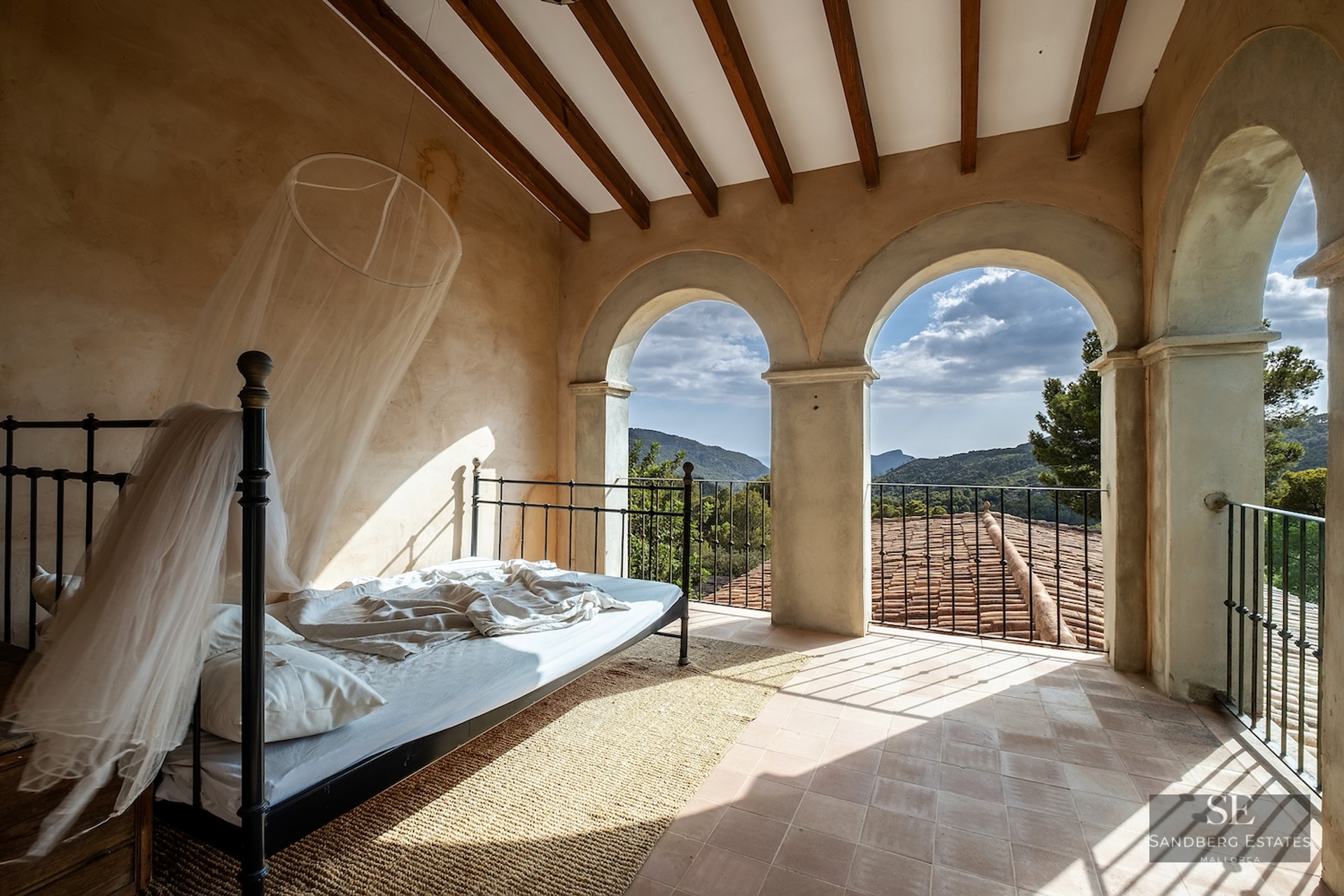 Wrought iron bed with mosquito net under stone arches overlooking scenic mountains.