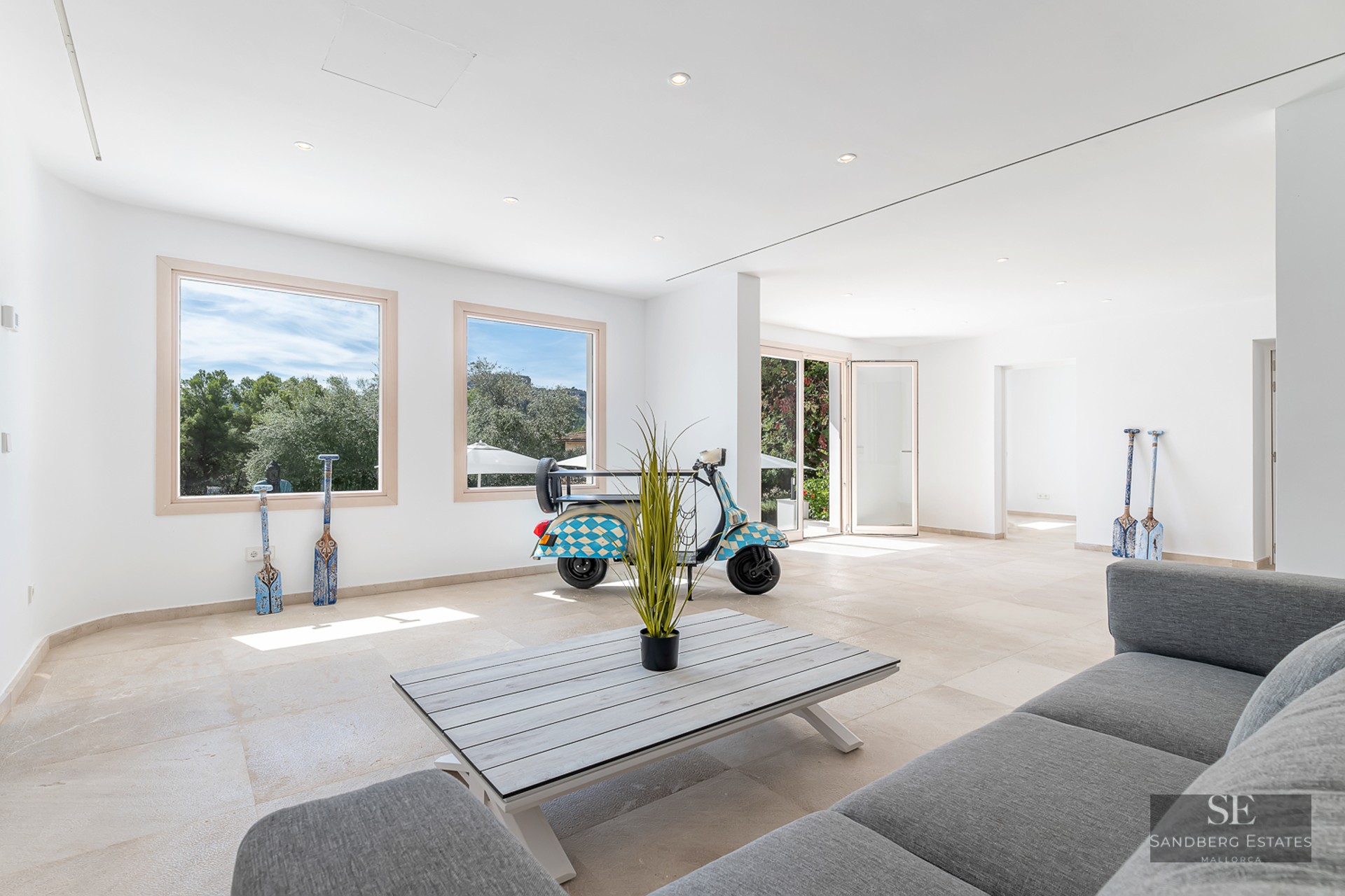 Bright living room with white walls, stone floors, a grey sofa, and a decorative blue-and-white tuk-tuk.