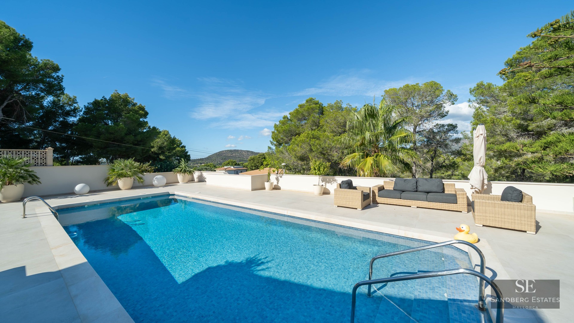 Piscine bleue sur une terrasse en pierre avec mobilier de salon en osier et vue sur la montagne.