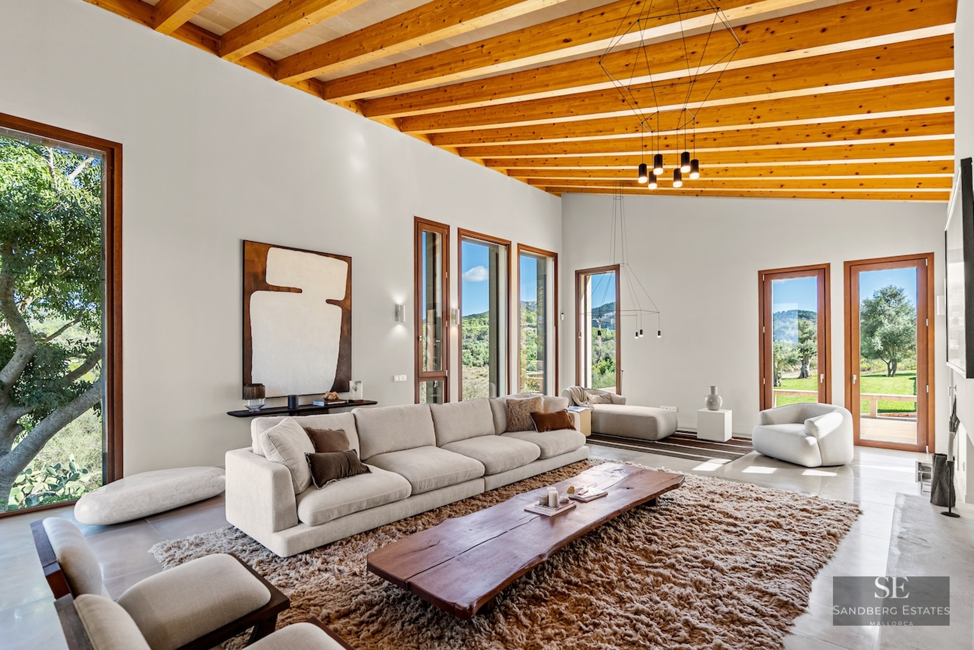 Bright living room with high wooden ceilings, cream sofa, live-edge wood table, and large windows viewing nature.