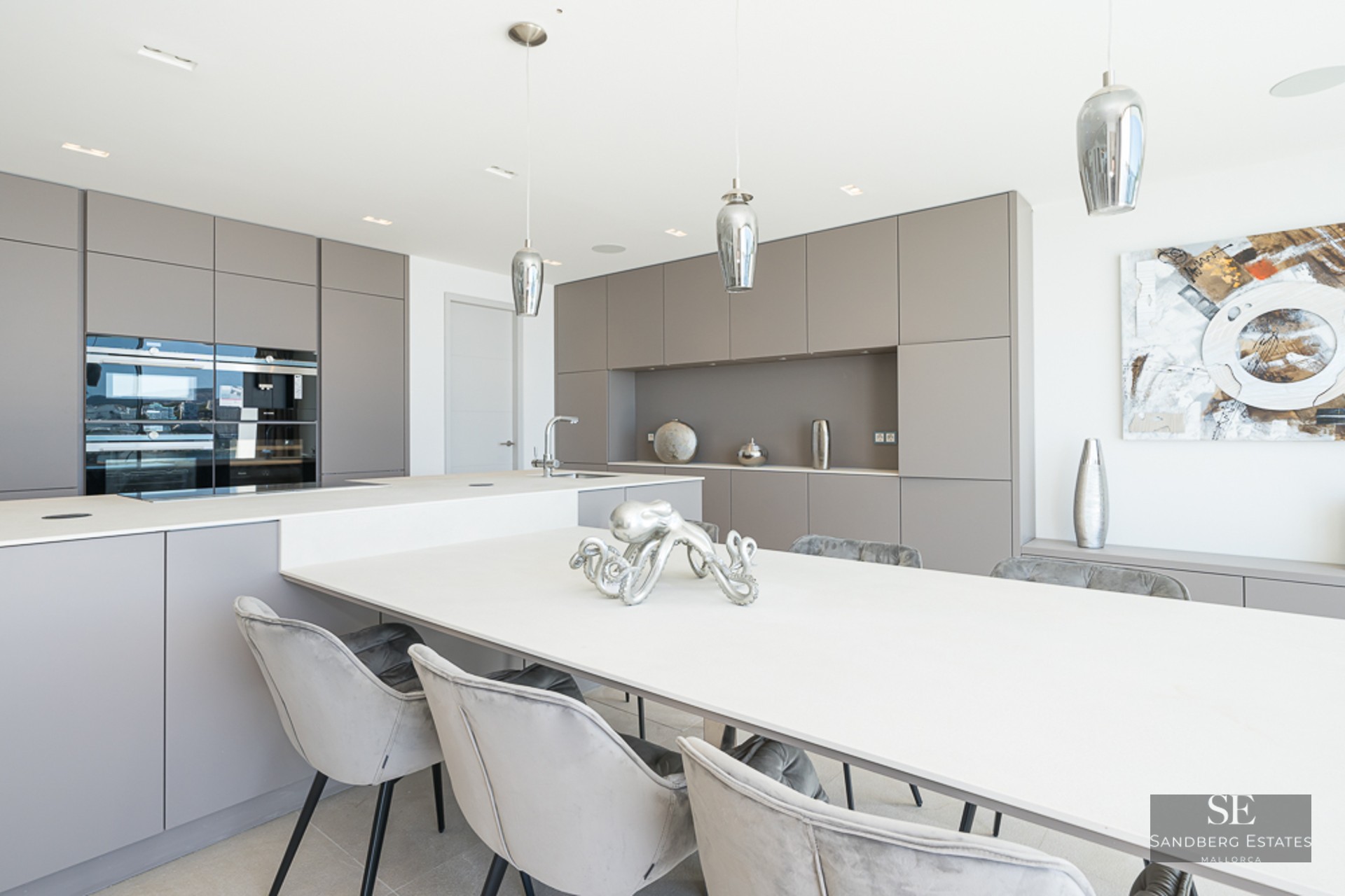 Contemporary kitchen with taupe cabinets, a large white island, and grey velvet dining chairs.