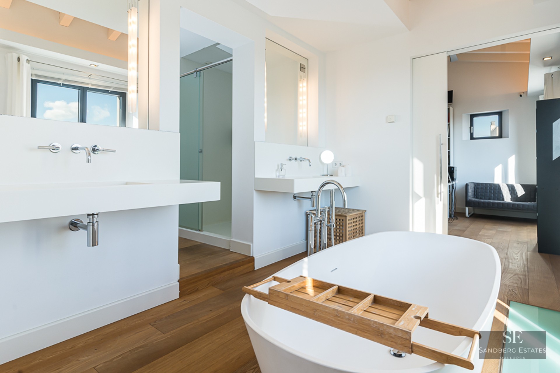 Bright master bathroom featuring a white freestanding bathtub, wooden floors, and modern floating sinks.