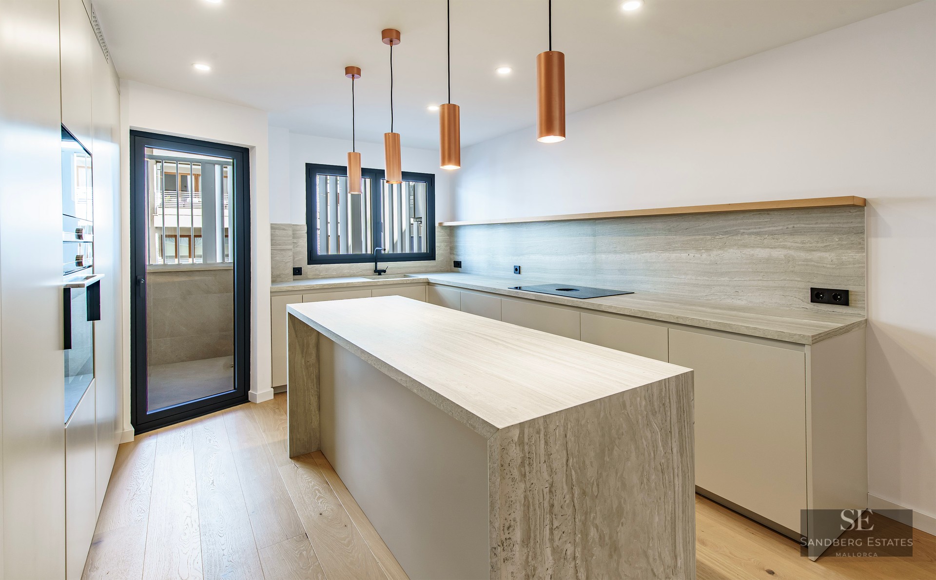 Cuisine lumineuse avec îlot en travertin, suspensions en cuivre et parquet en bois clair.