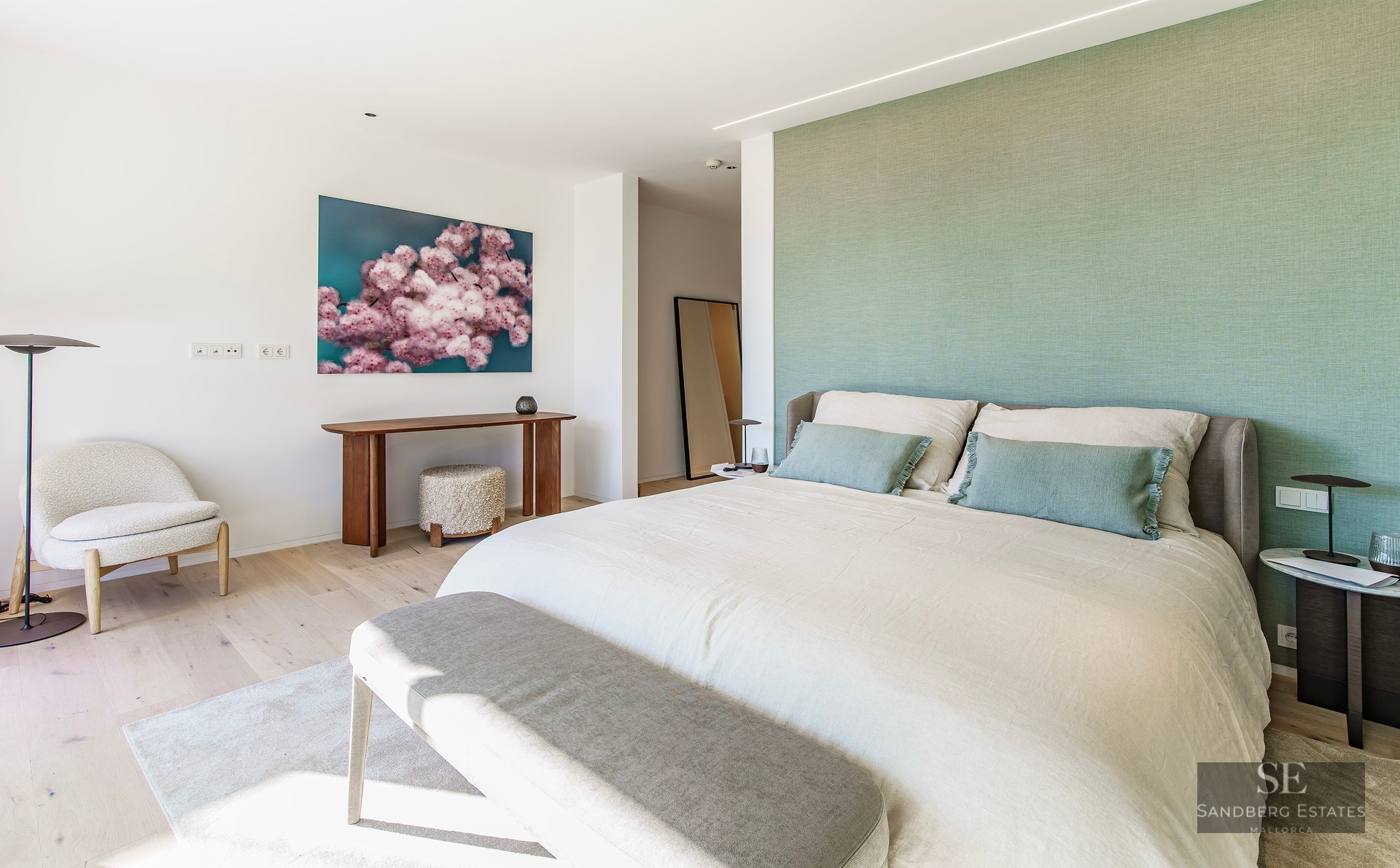 Bright master bedroom featuring a sage green wall, large bed, and designer furniture on light wood floors.