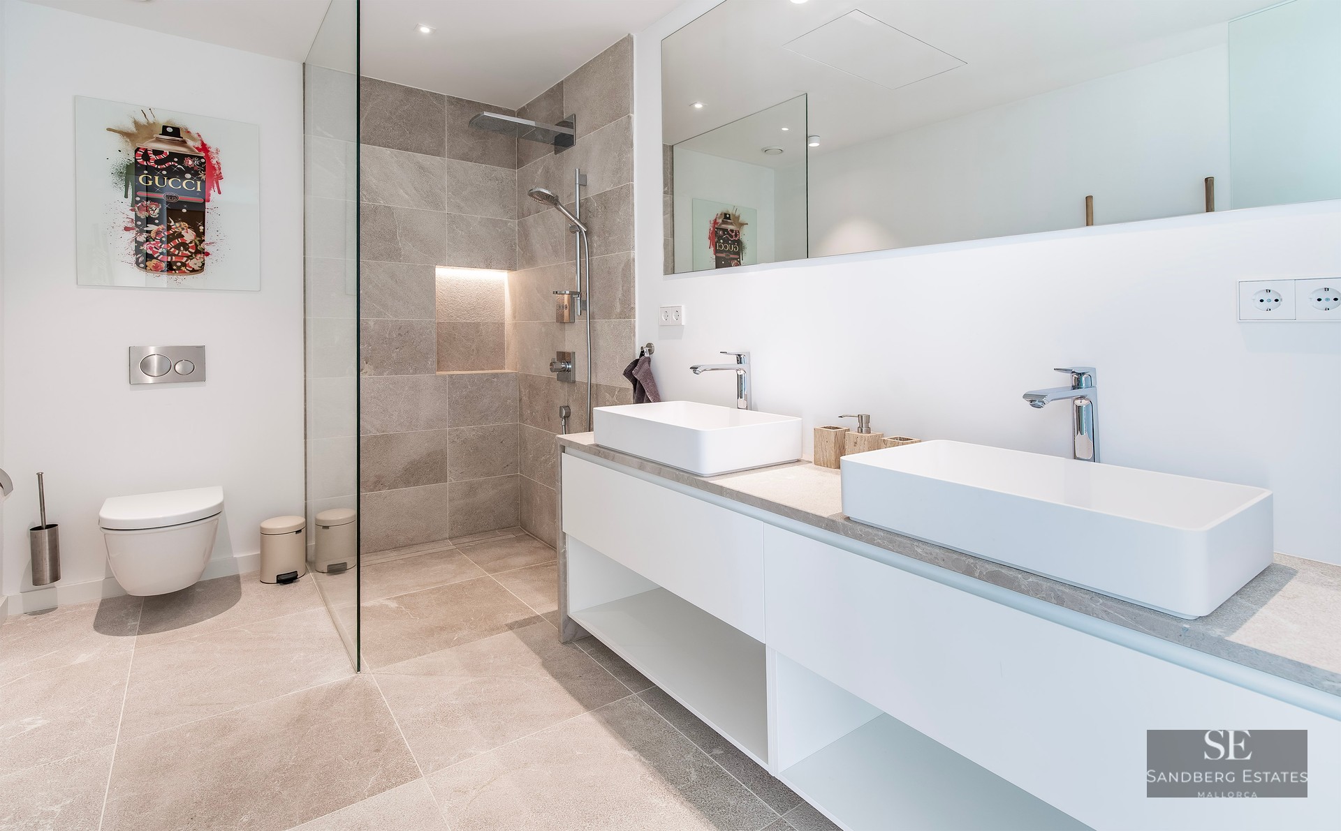 Bright bathroom featuring a double white vanity, glass walk-in shower with grey tiles, and a wall-hung toilet.
