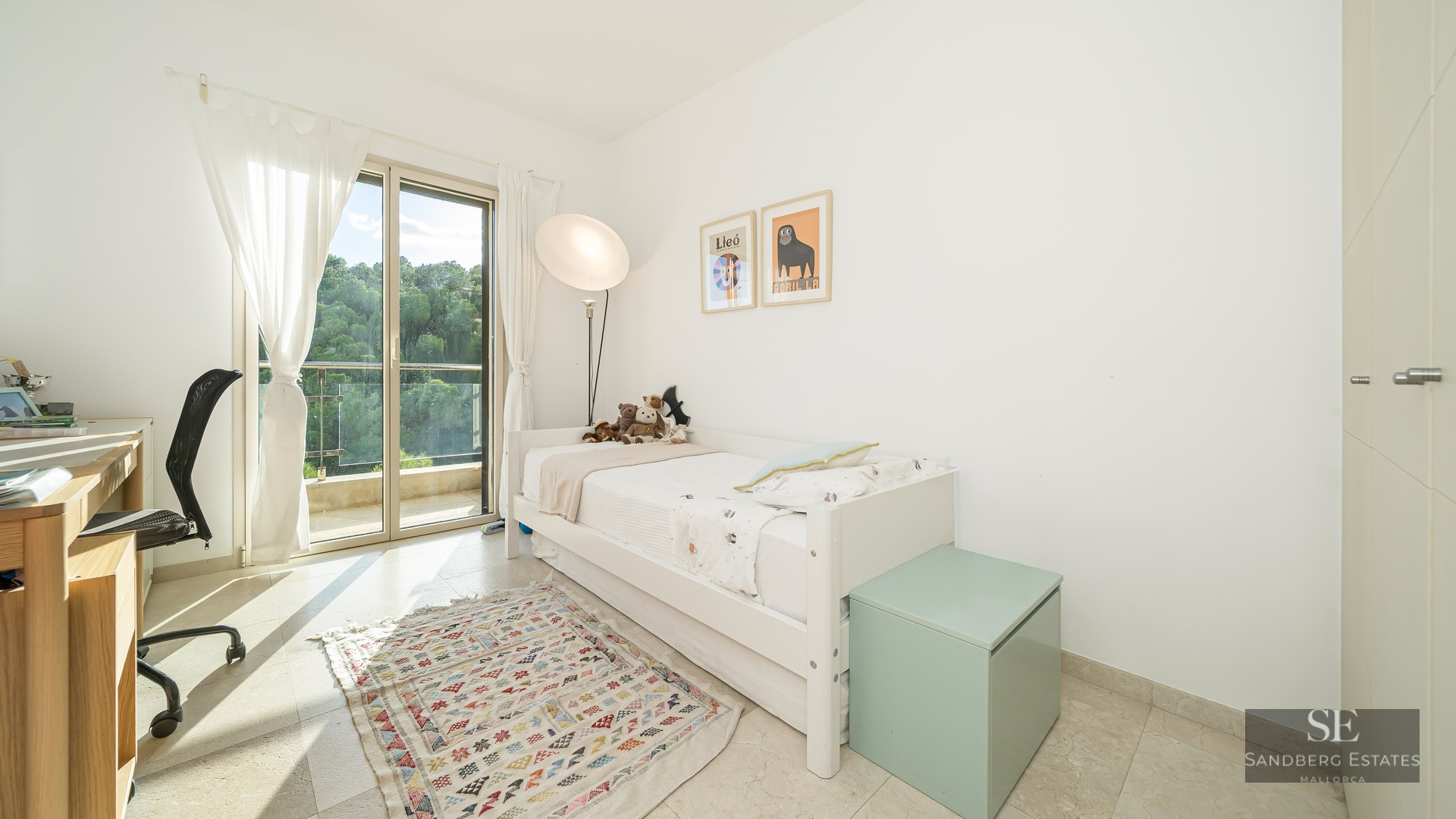 White bedroom featuring a single bed, desk, sliding glass door to a balcony, and a geometric rug.