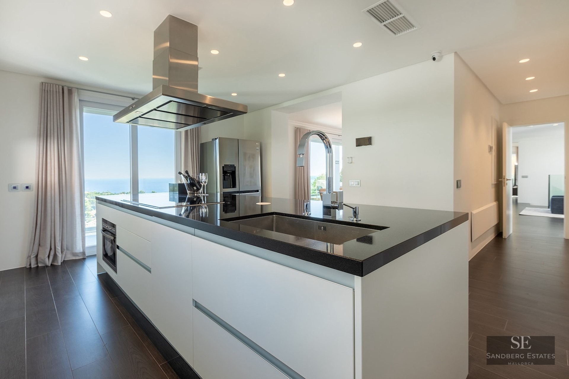 Modern kitchen featuring a black island, stainless steel hood, and floor-to-ceiling windows with a sea view.