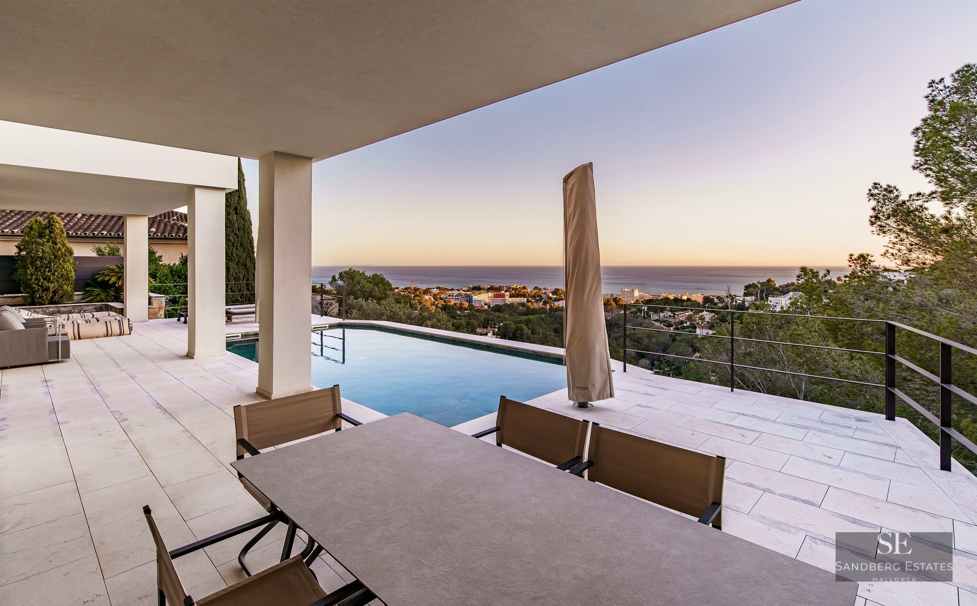 Modern terrace with an infinity pool, outdoor dining area, and panoramic sea views at sunset.