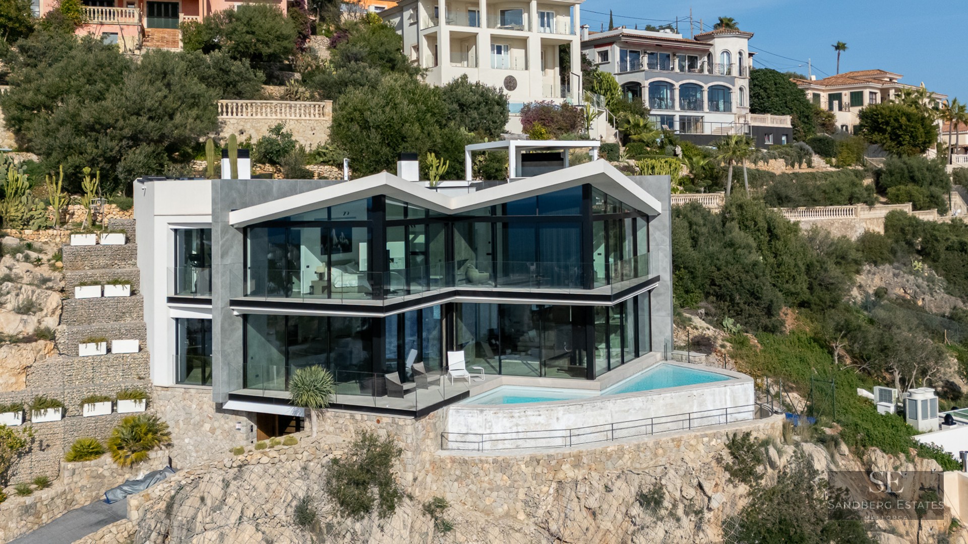 Modern glass villa built into a rocky hillside featuring an angular roof and a small infinity pool on the terrace.