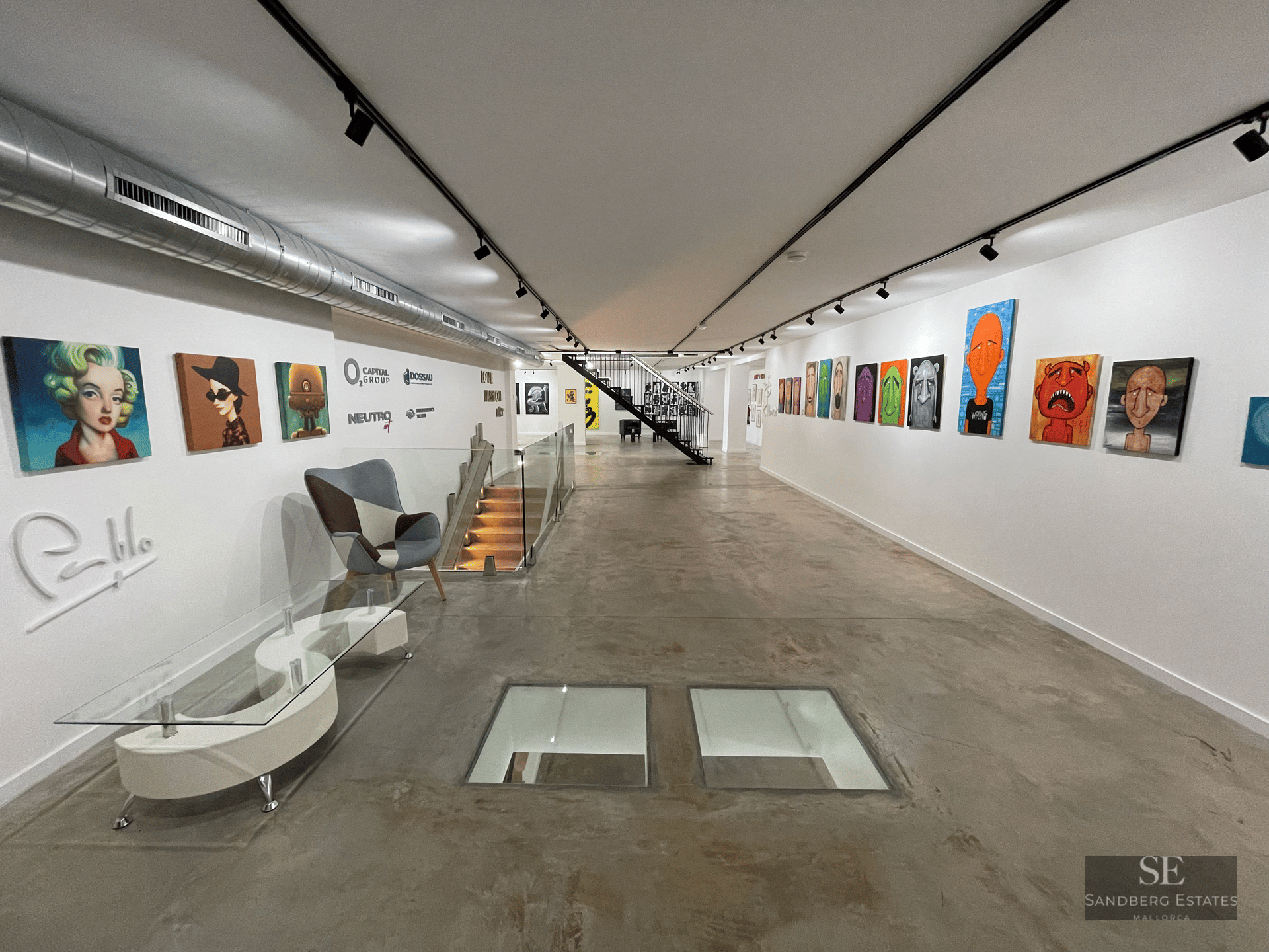 A long industrial gallery with polished concrete floors, white walls filled with pop art, and glass floor inserts.