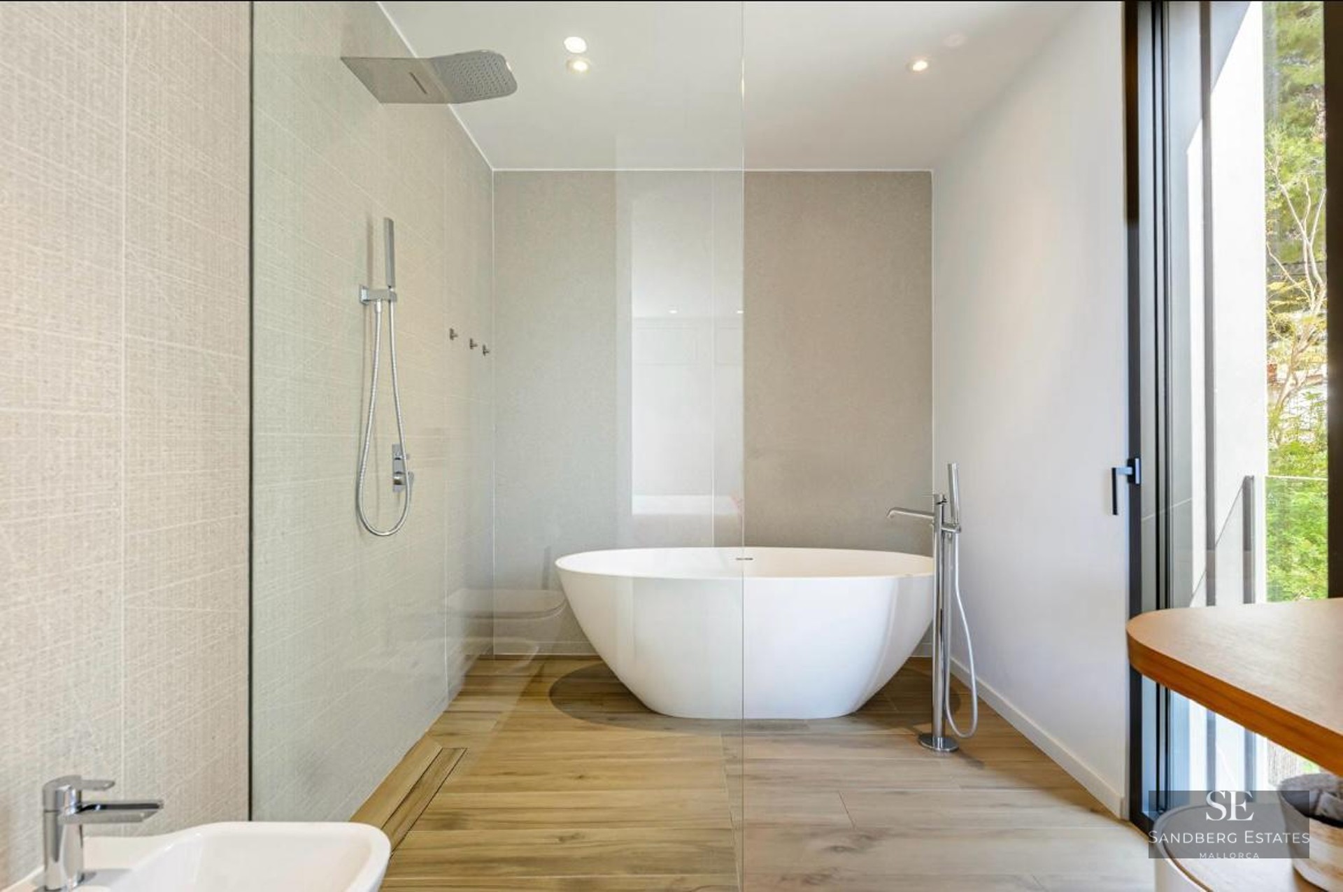 Luxury bathroom featuring a white freestanding bathtub, glass shower partition, and wood-look flooring.