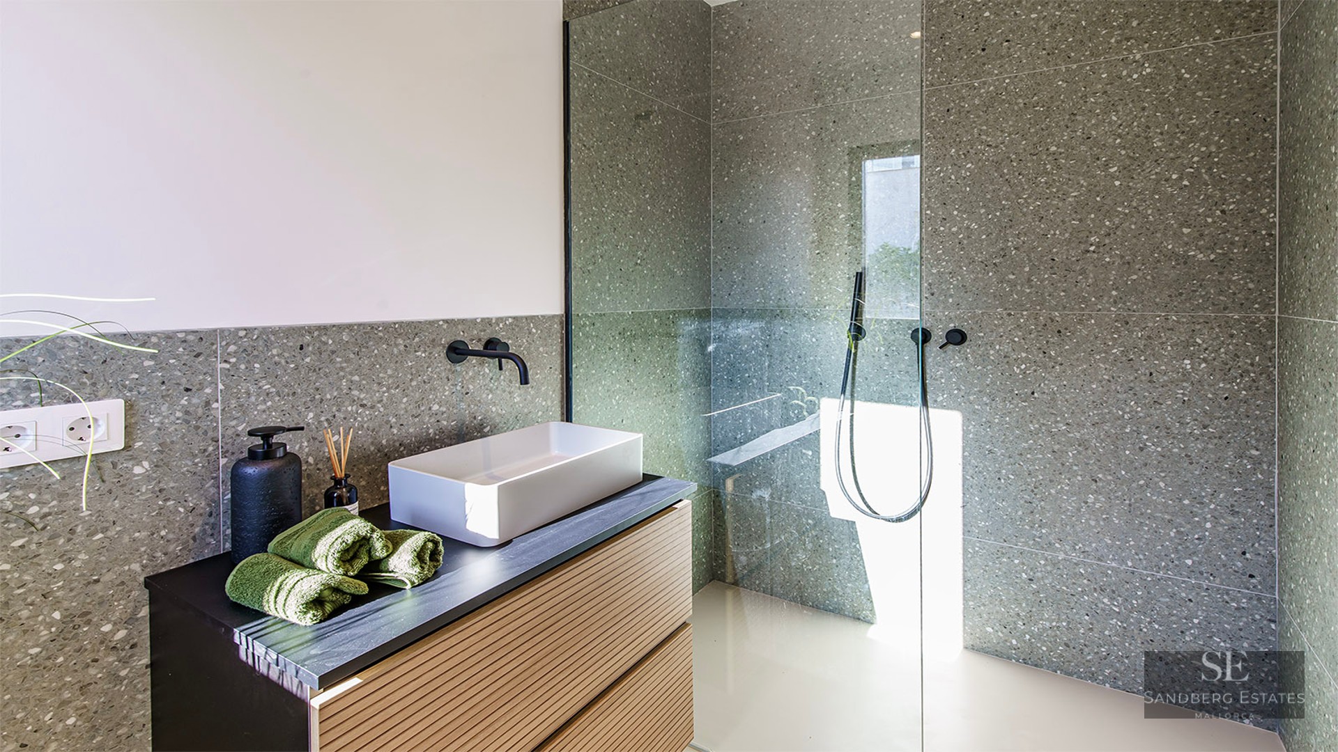 Modern bathroom featuring speckled grey tiles, a white vessel sink on a wooden vanity, and a glass-enclosed shower.