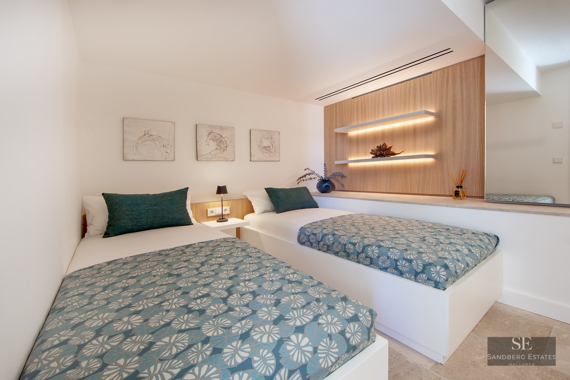 Modern bedroom featuring two single beds with teal patterned covers, wooden wall panels, and warm LED floating shelves.