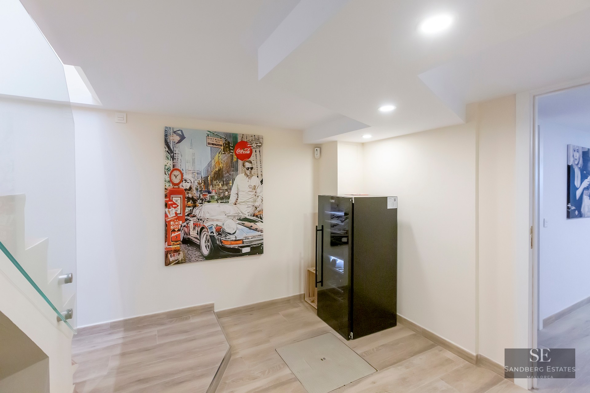 Modern interior landing with a large pop-art painting of a car, a black wine cooler, and glass stairs.