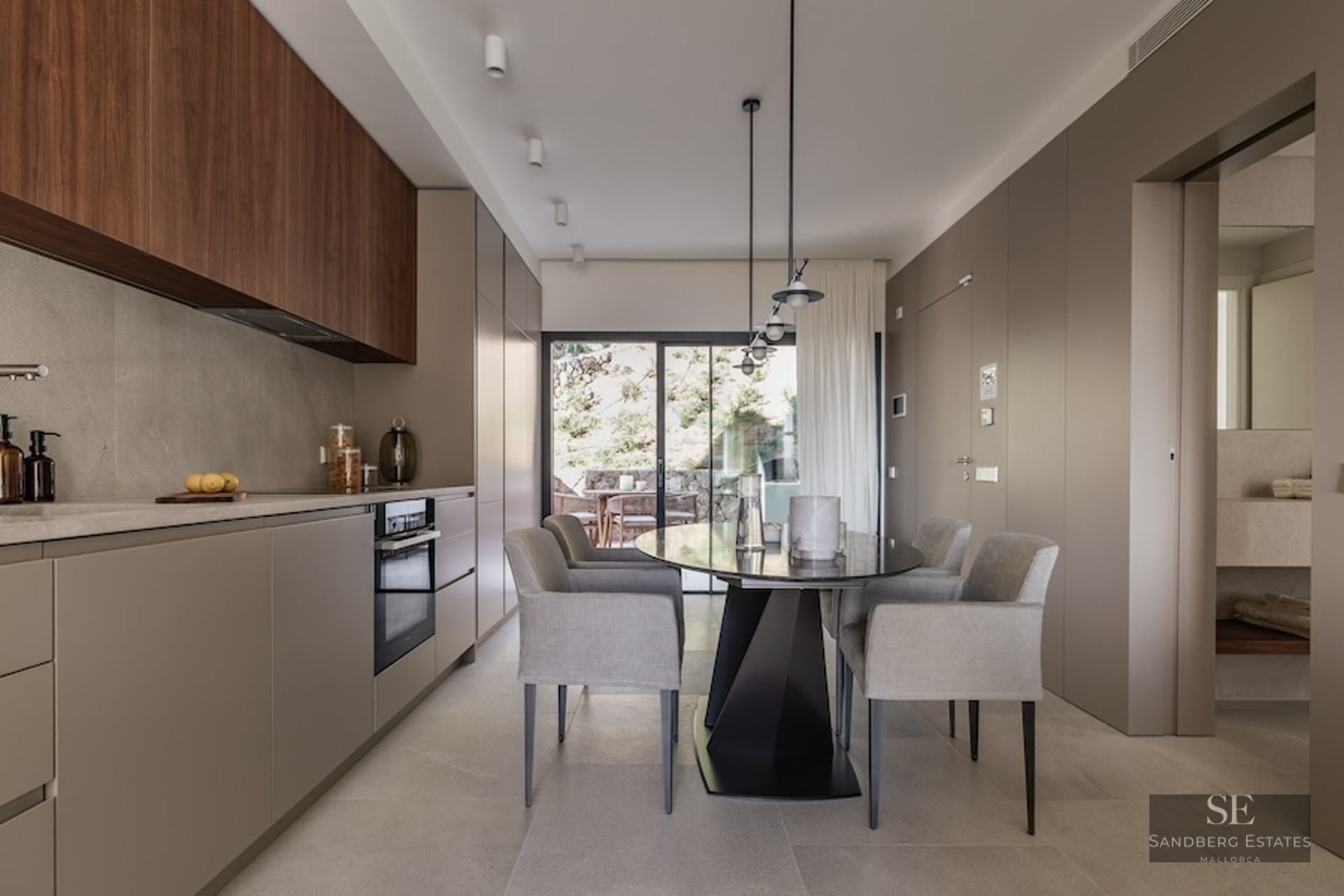 Minimalist kitchen with taupe and wood cabinetry, a grey dining table, and large glass doors leading to a terrace.