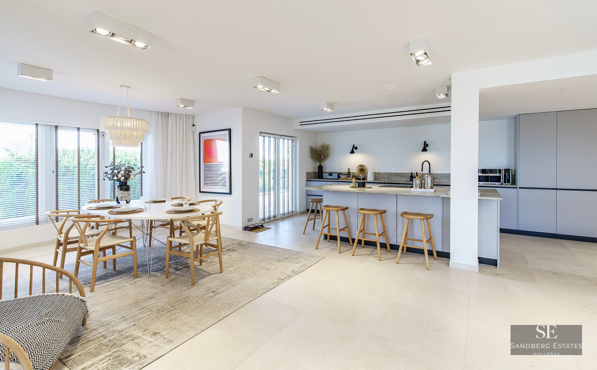 Spacious kitchen featuring a stone island and wooden stools next to a dining area with a round white table and designer chairs.