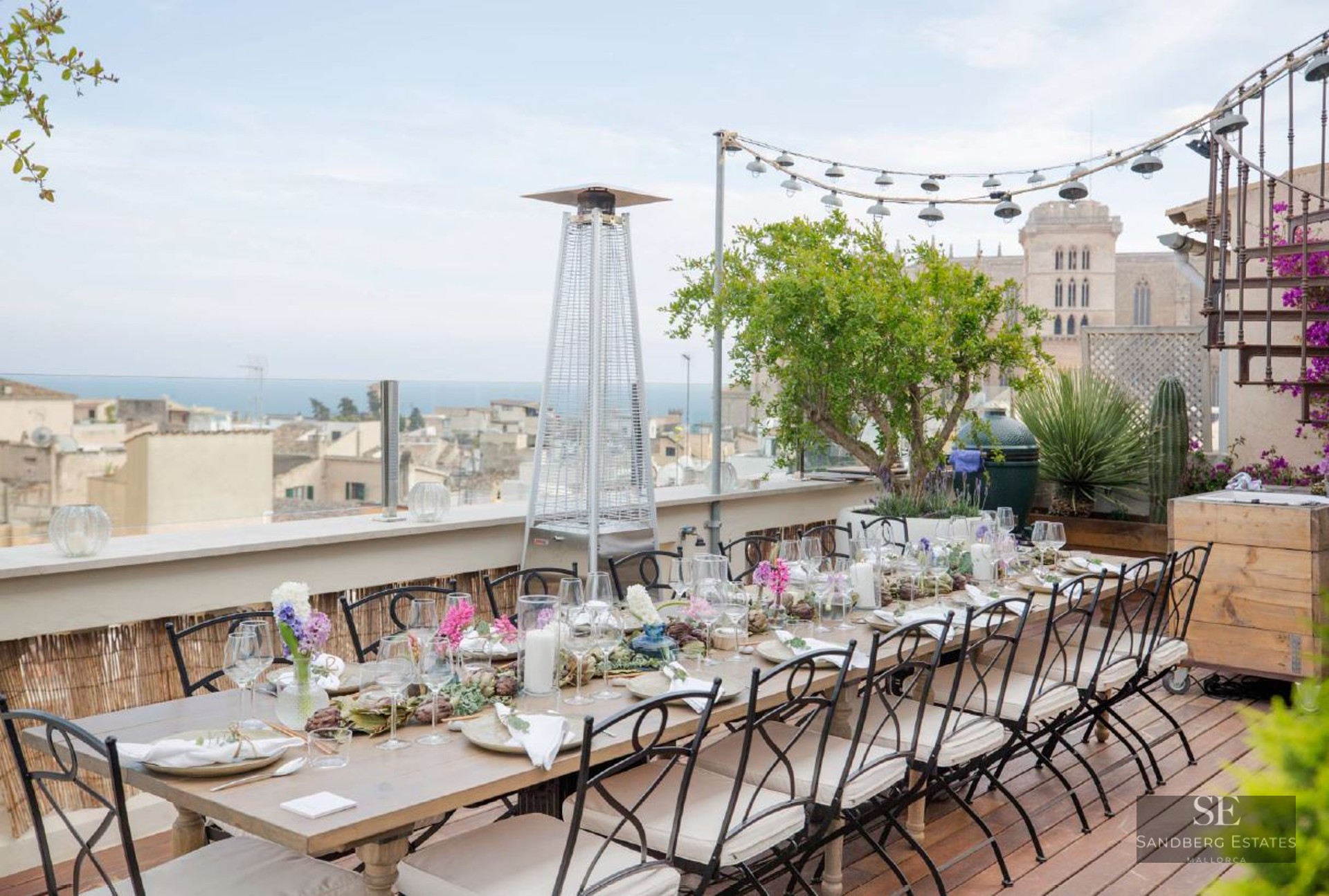 An elegantly set dining table on a wooden deck terrace overlooking a historic city and the sea.