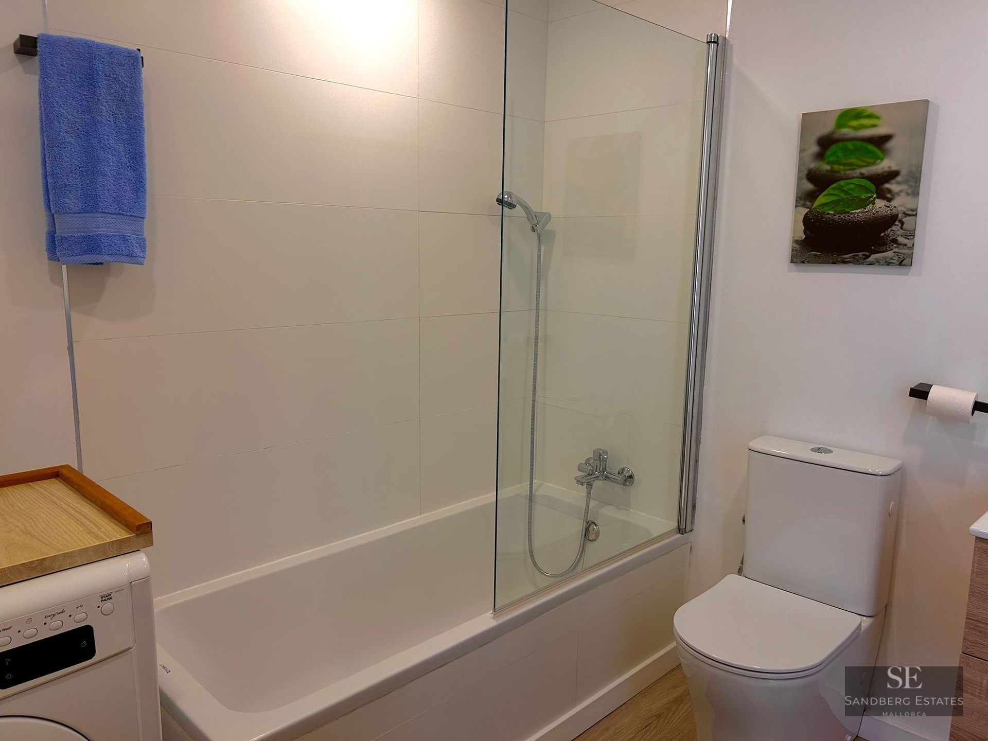 White bathroom featuring a bathtub with glass partition, toilet, and washing machine.