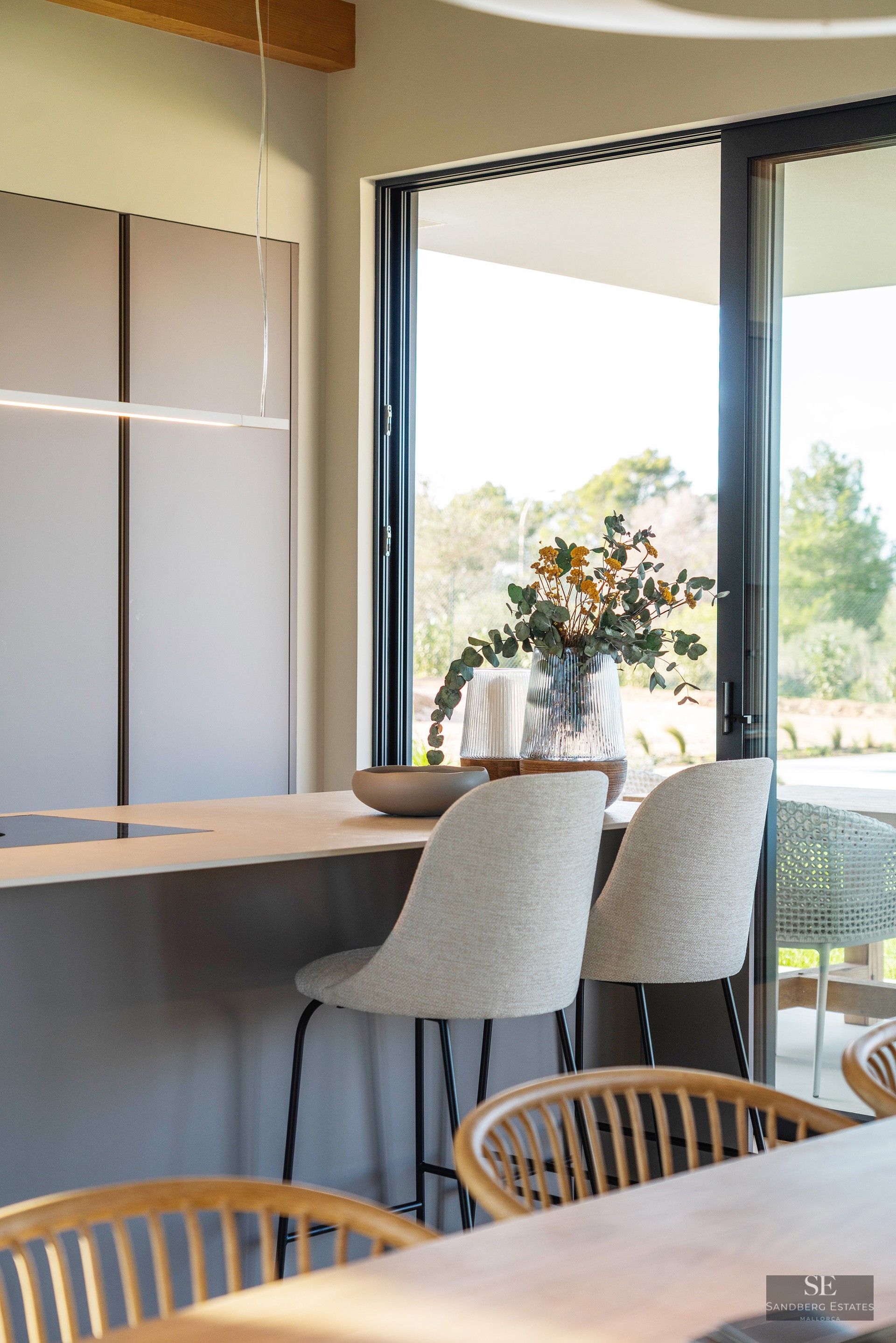 Modern kitchen island with grey bar stools next to a large glass door overlooking a garden.
