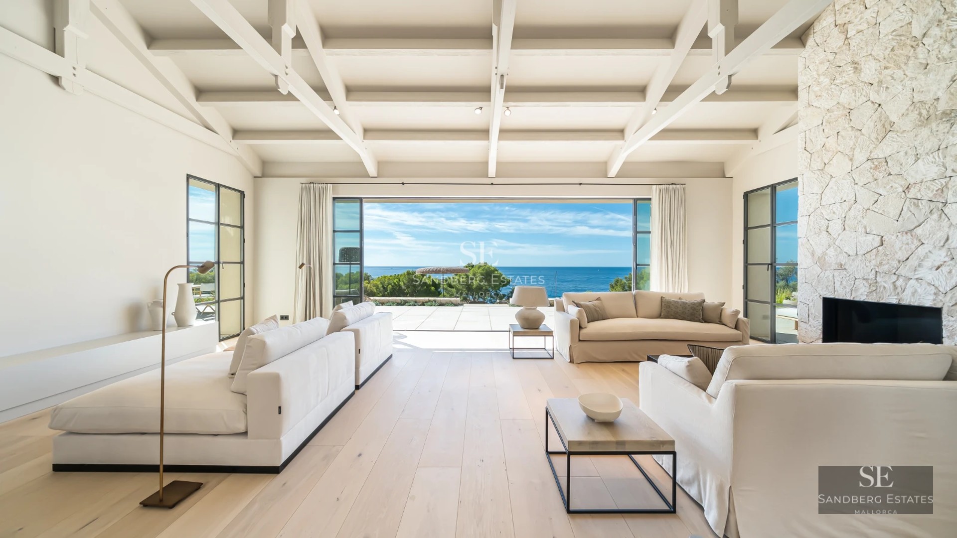 Spacious living room with panoramic windows, light wood floors, modern fireplace, and access to a sea-view terrace. Designer furniture and natural light.