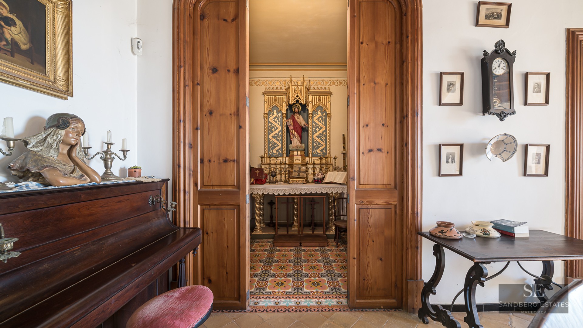 View through wooden doors into a small ornate private chapel with an altar next to an upright piano.