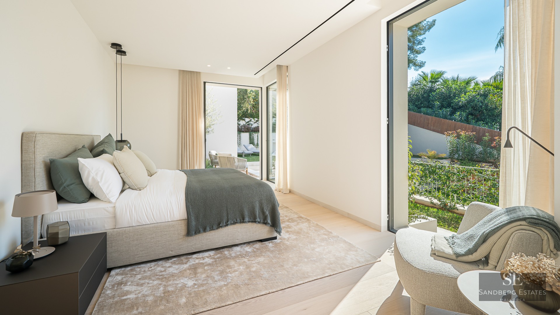 Modern master bedroom with large bed, floor-to-ceiling windows, and views of a lush garden.