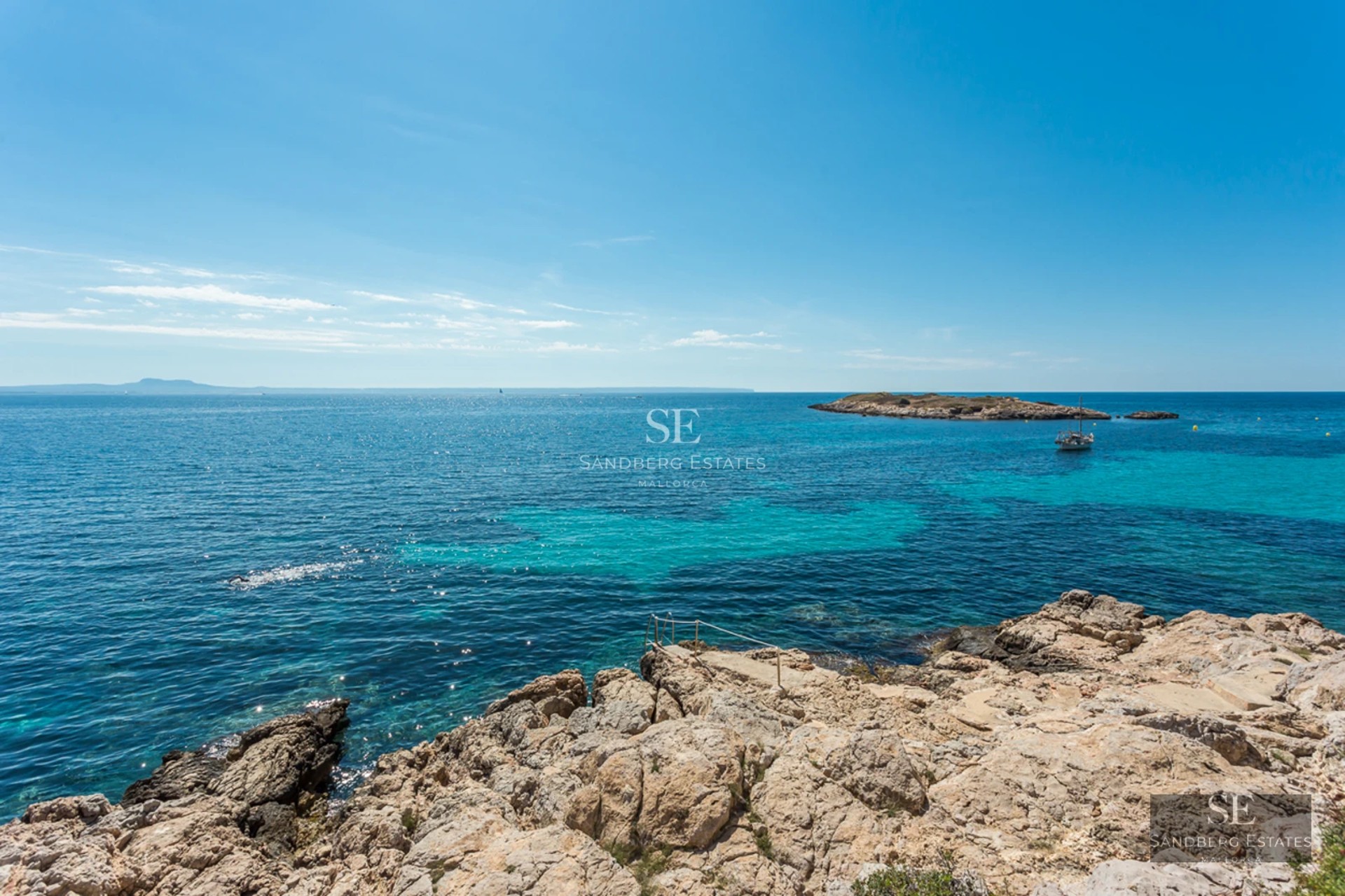 Panoramic view of turquoise Mediterranean waters from a rocky shore with a small island and boat in the distance.