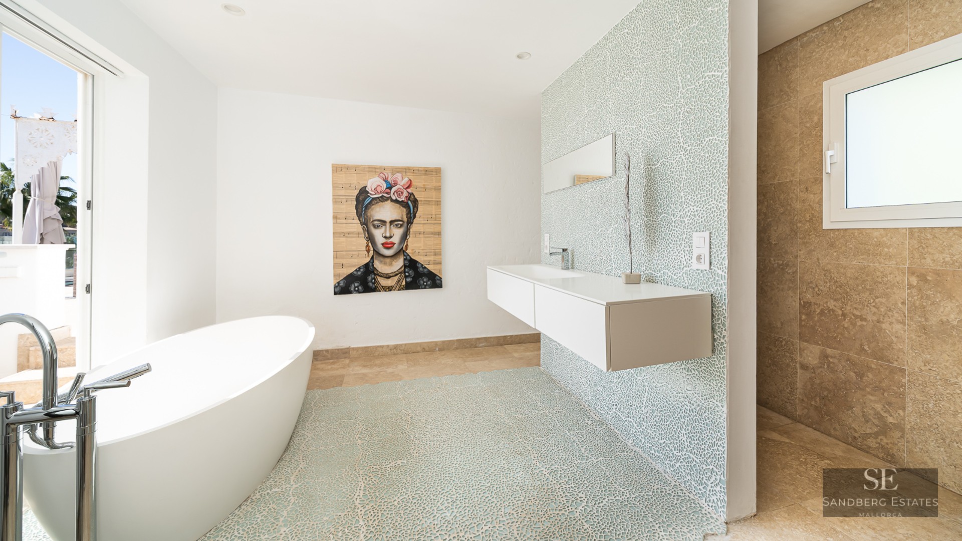 Bright bathroom featuring a white oval tub, floating vanity, blue mosaic wall, and a Frida Kahlo portrait.