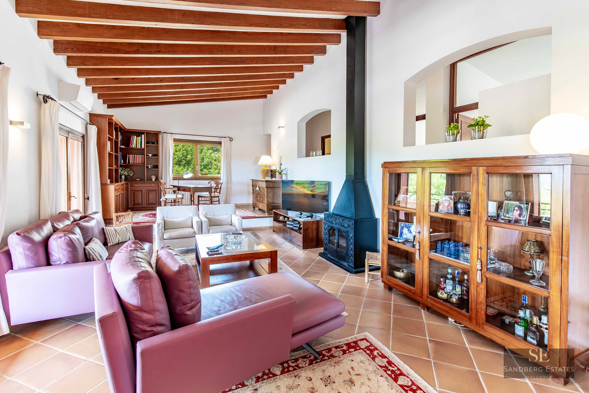 Spacious living room featuring wood ceiling beams, purple sofas, a fireplace, and terracotta flooring.
