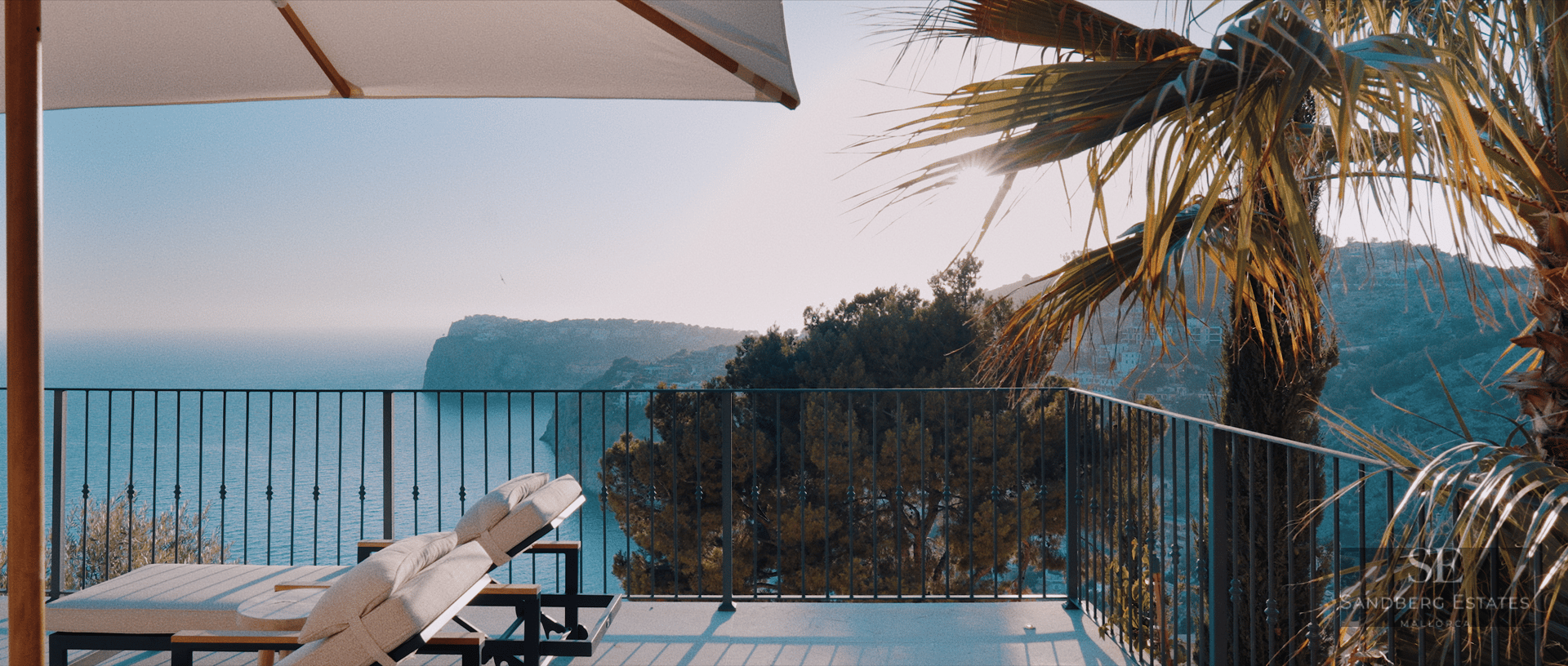 Sun loungers on a modern terrace overlooking a coastal bay and cliffs under a clear blue sky.