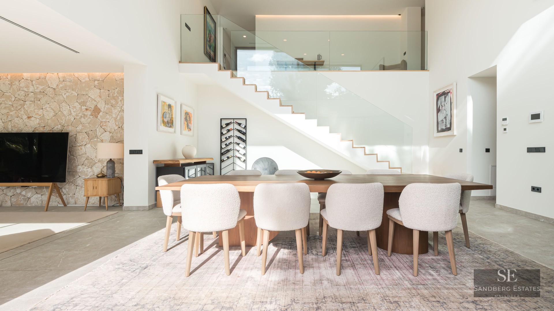 Salle à manger minimaliste avec table en bois, chaises blanches en bouclé et escalier en verre moderne.