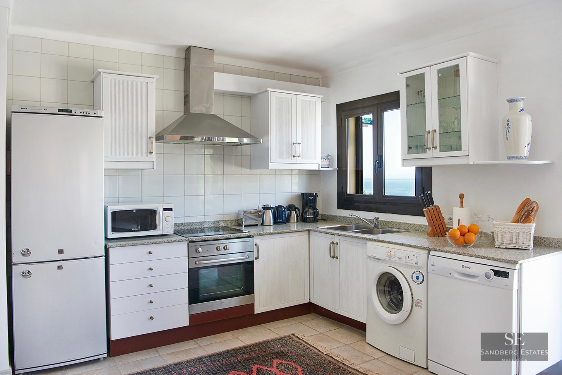 White kitchen with granite countertops, stainless steel appliances, and a window overlooking the ocean.