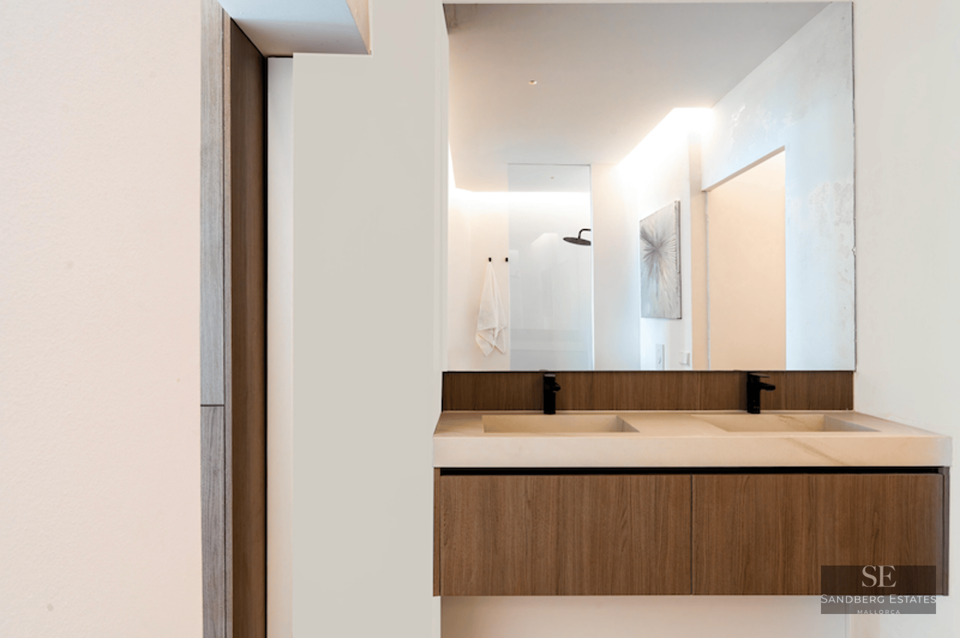 Floating wood bathroom vanity with two sinks and matte black faucets beneath a large frameless mirror.