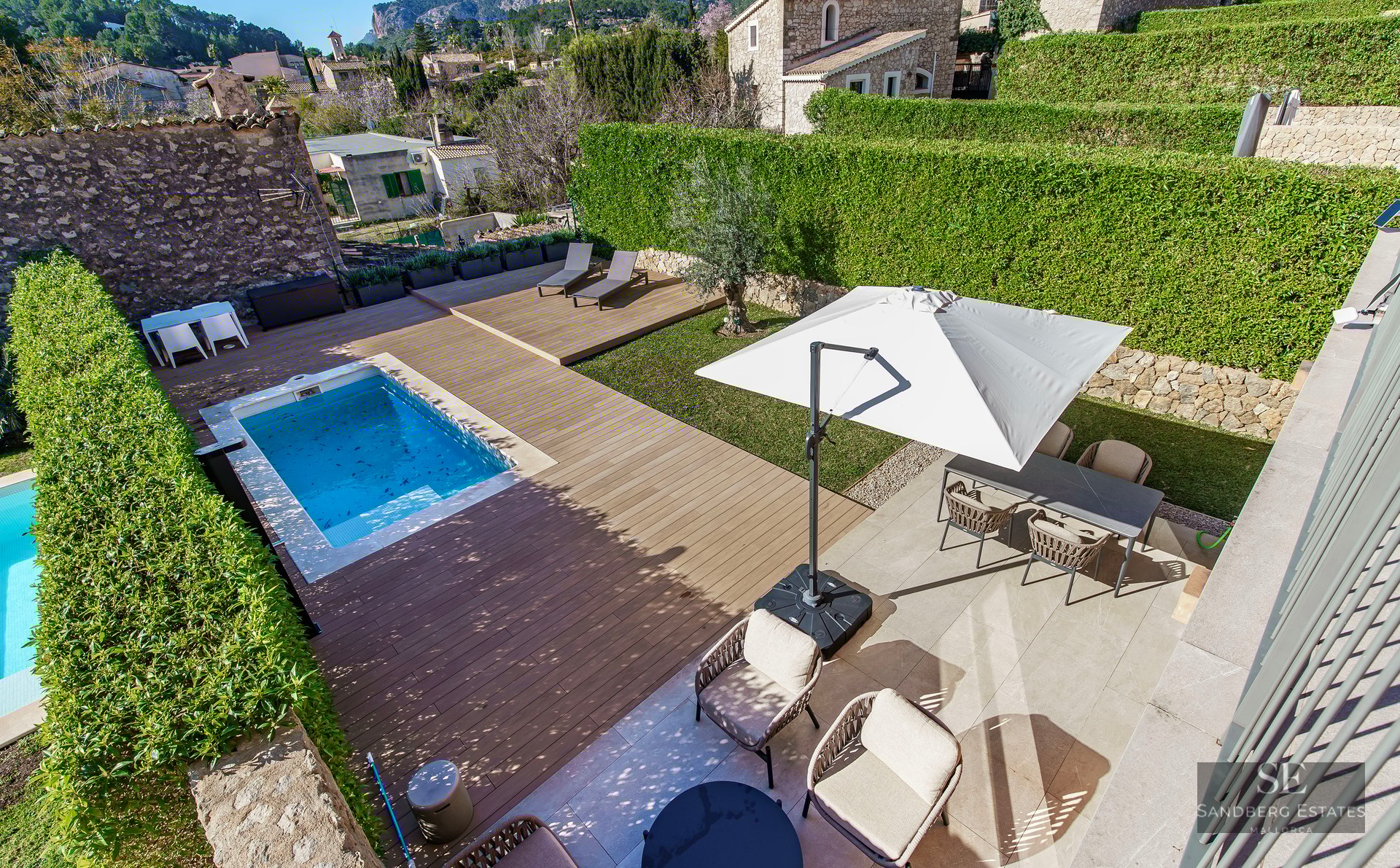 Overhead view of a rectangular swimming pool, wooden deck, lawn, and outdoor dining area surrounded by privacy hedges.