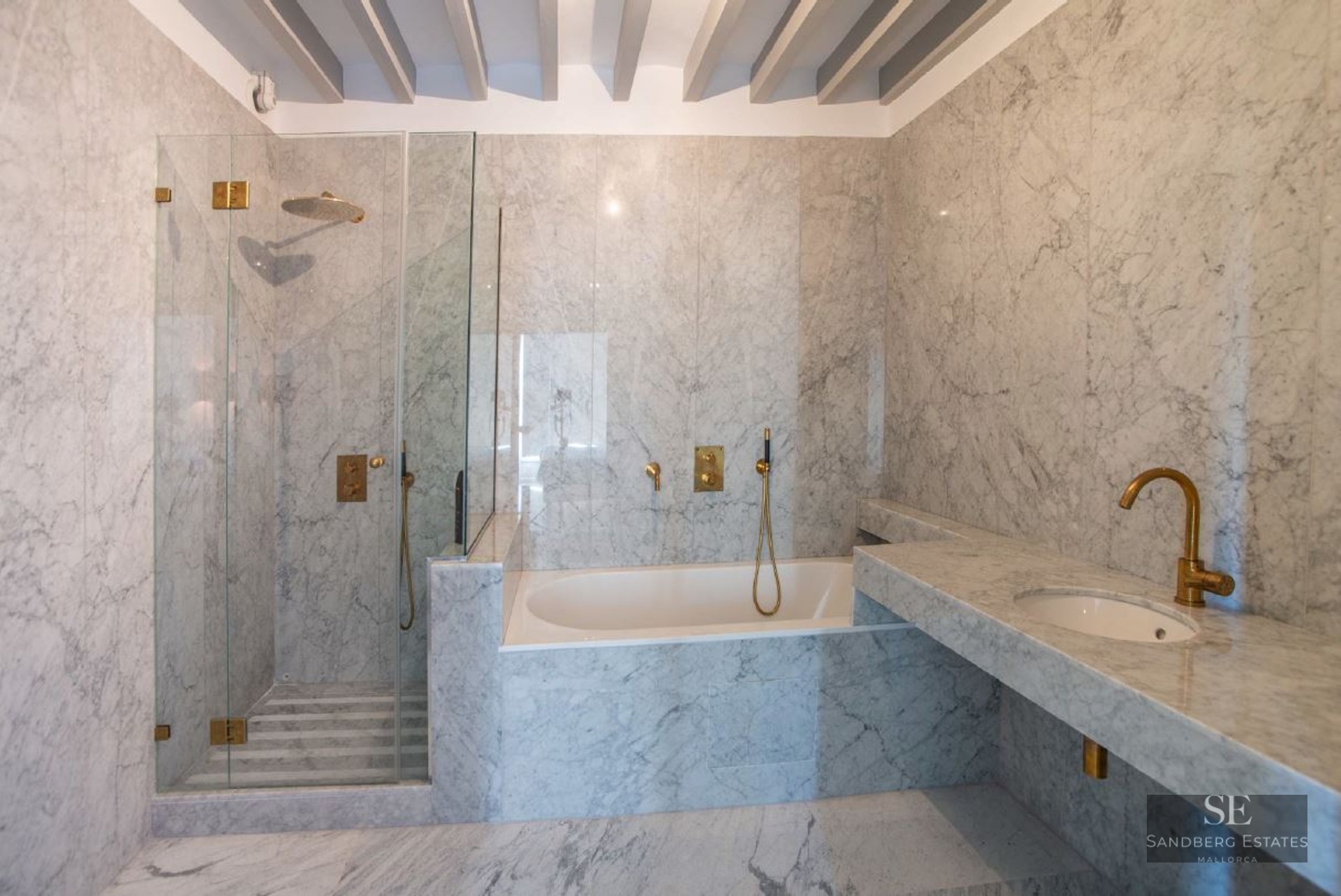 A high-end bathroom featuring marble walls and floors, a glass walk-in shower, a built-in tub, and brass faucets.