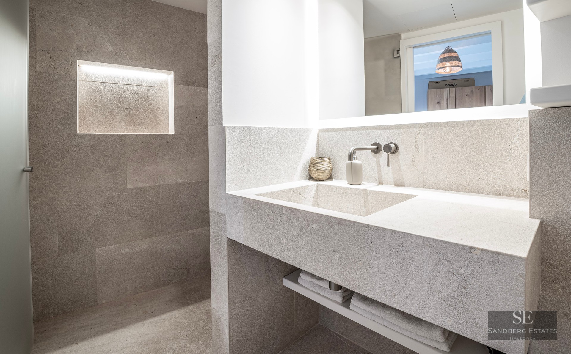 Salle de bain moderne en pierre avec vasque intégrée, robinet mural et niche murale éclairée.