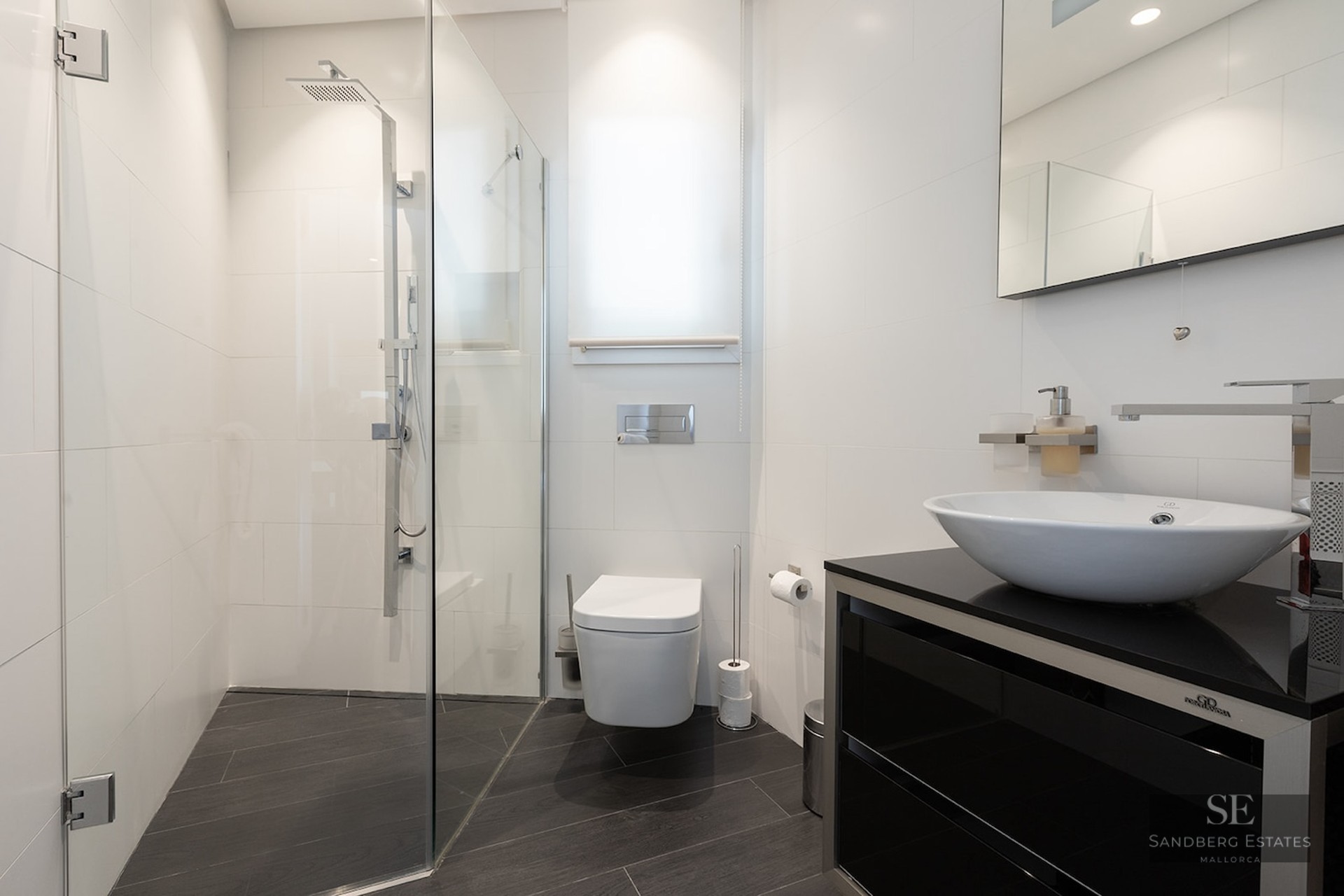 Contemporary bathroom featuring white tiles, walk-in glass shower, wall-mounted toilet, and vessel sink on black vanity.