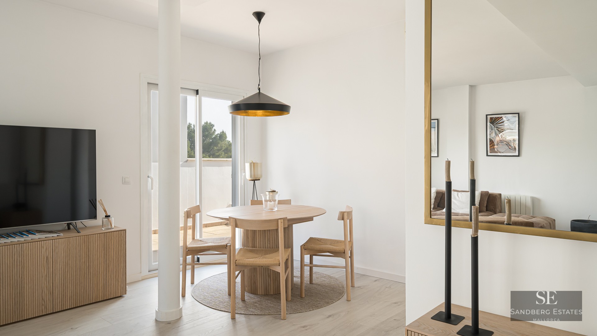 Bright dining area featuring a round wooden table, wicker chairs, black pendant lamp, and terrace access.