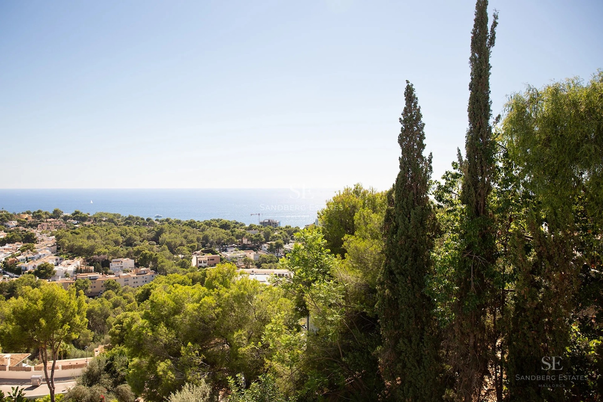 Panoramic view of the blue Mediterranean Sea over a lush green forest and coastal town under a clear sky.